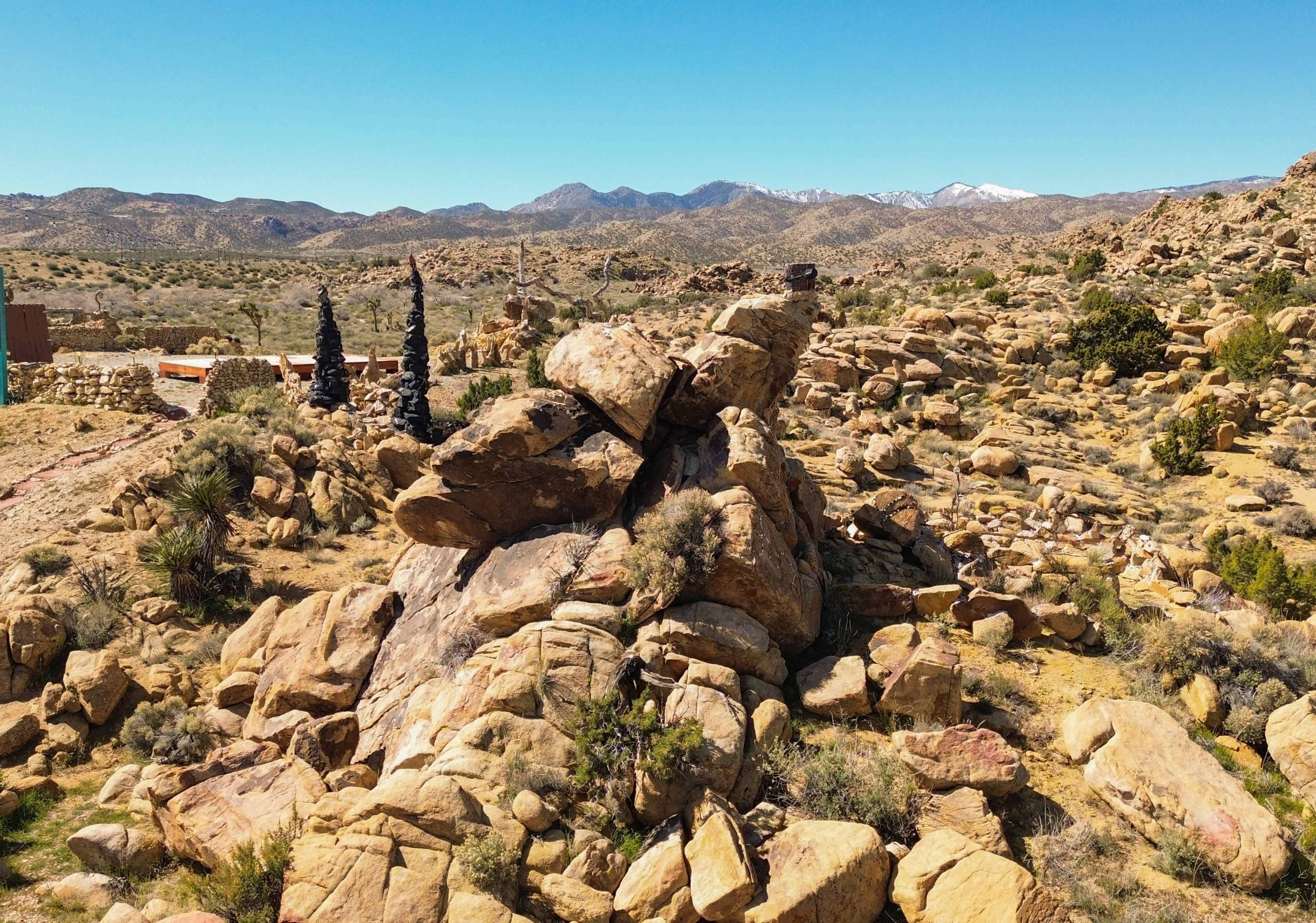 A rugged landscape features large boulders amidst sparse vegetation and distant mountains.