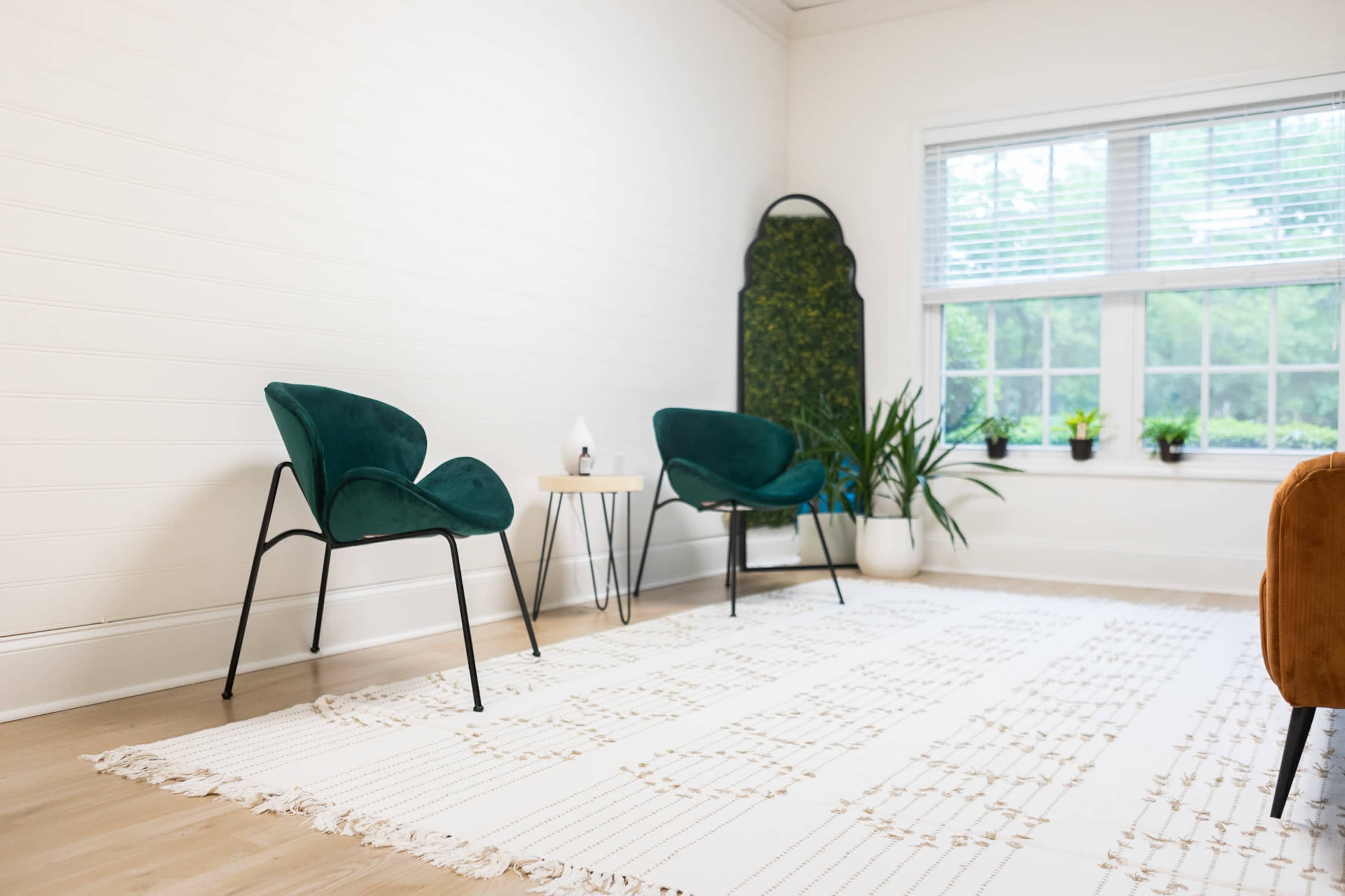 The image shows a bright room with two green chairs, a small table, a potted plant, and a large window with natural light.