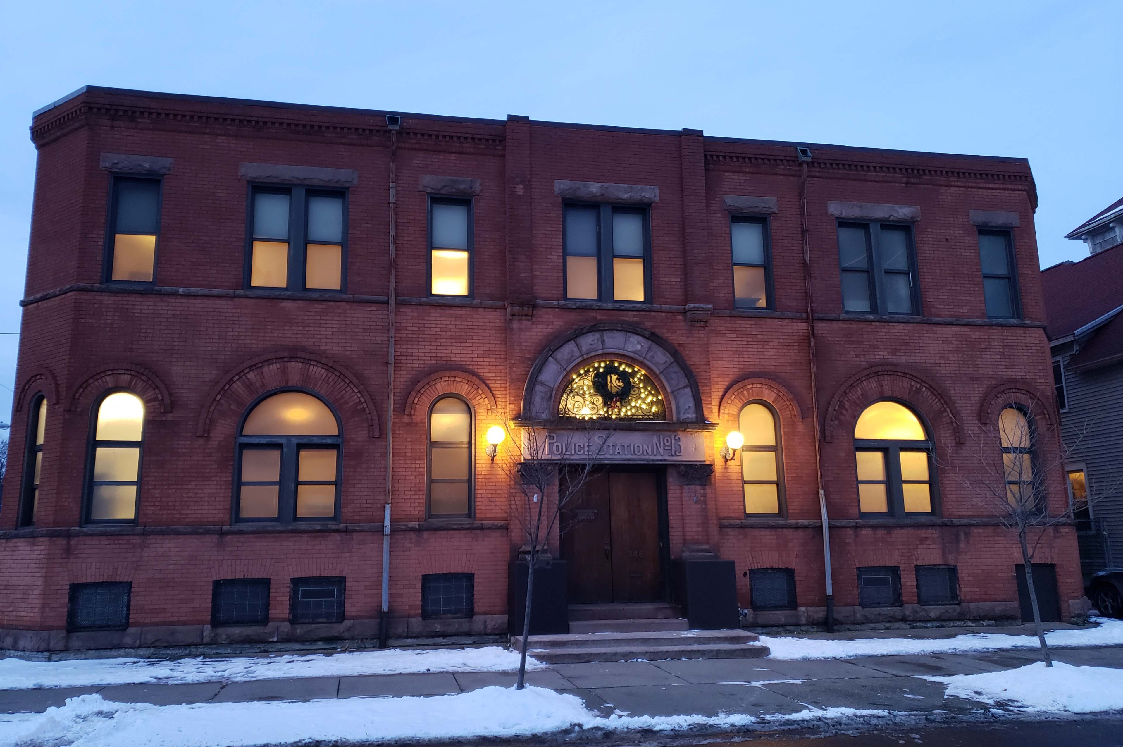 The brick building features arched windows and a decorative clock above the main entrance, illuminated in the evening.