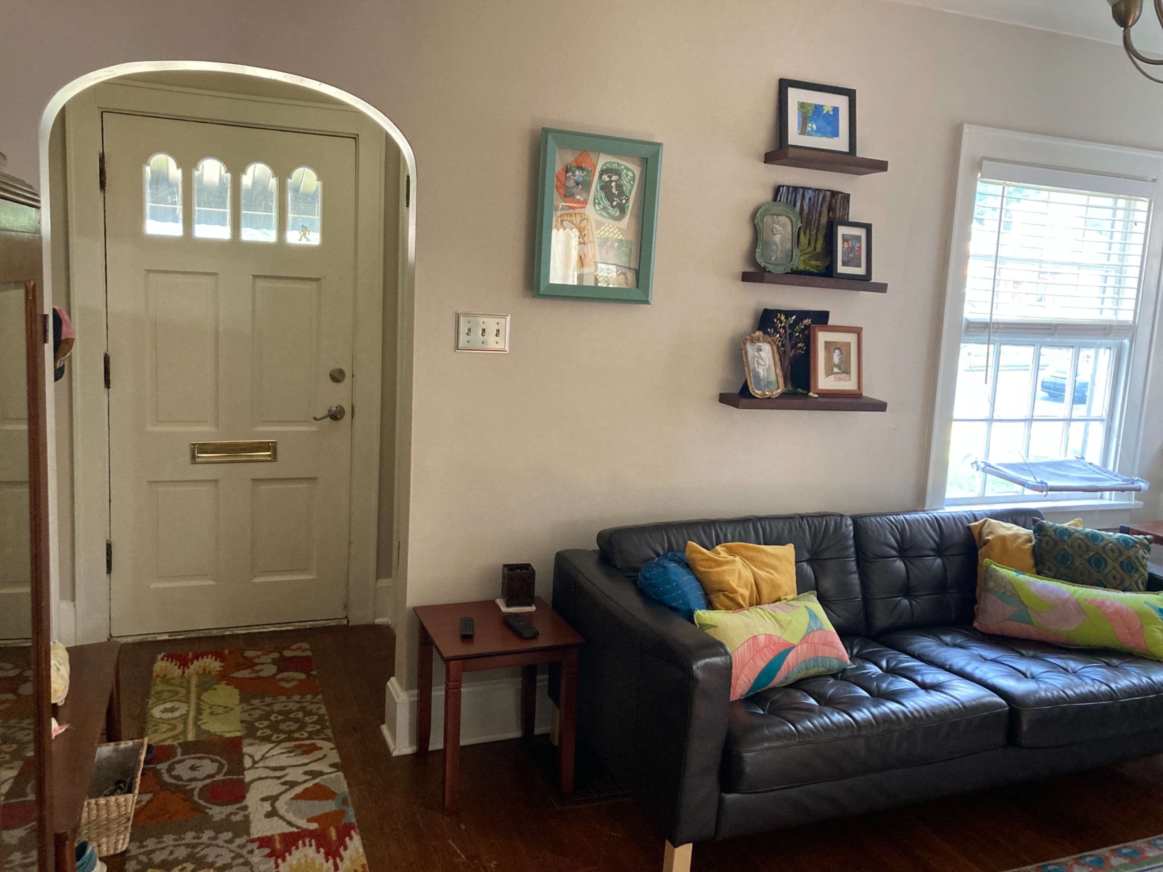 A living room with a dark leather couch adorned with colorful cushions, a wooden side table, and a doorway leading outside.