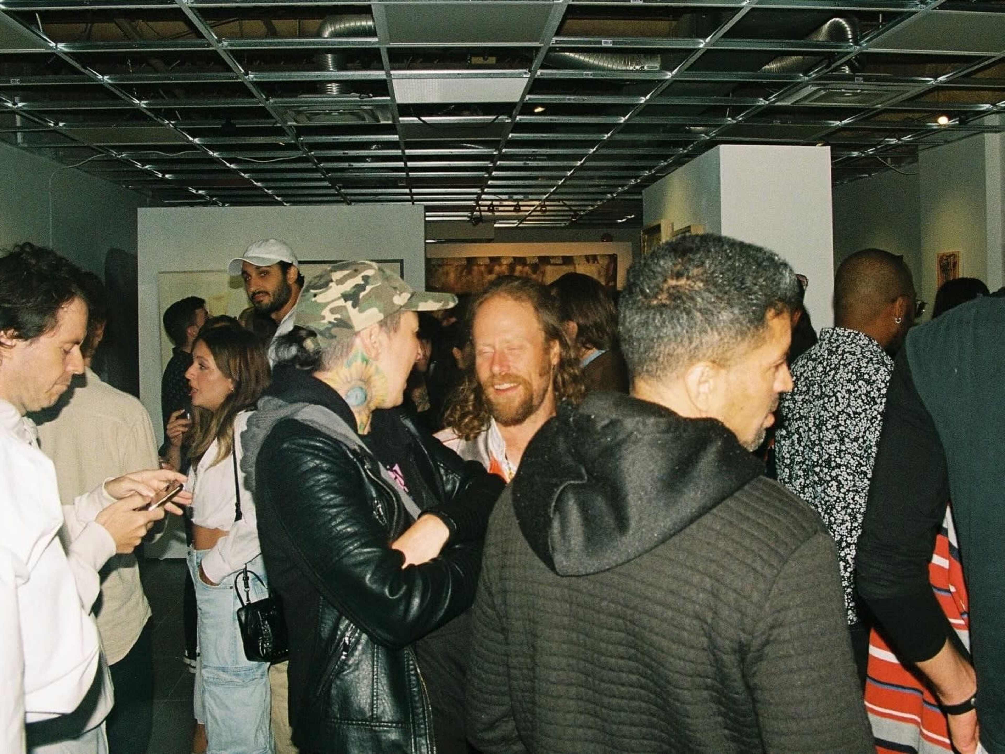 A group of people socialize at an indoor event with art displayed on the walls.