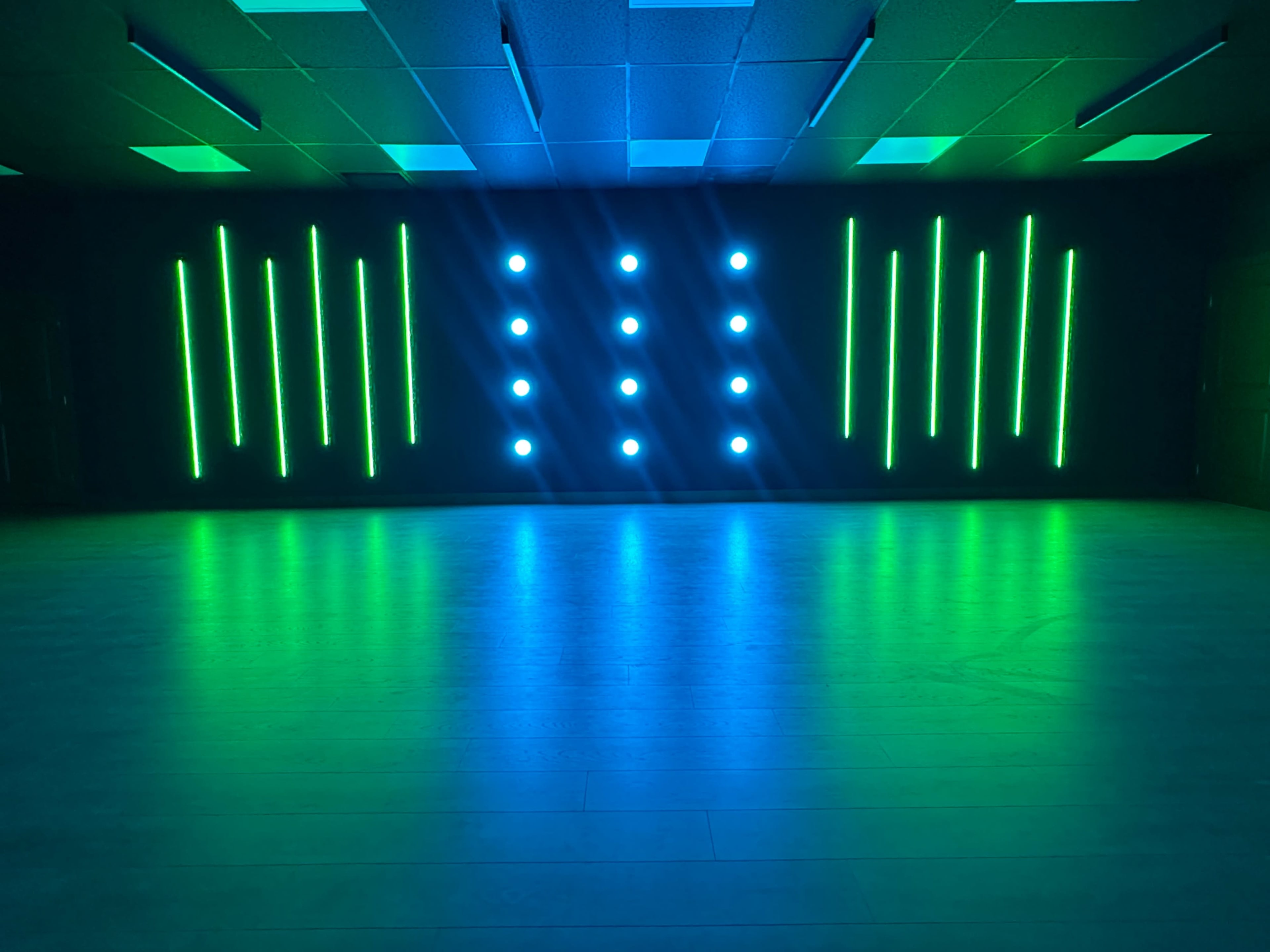 A stage with vertical LED lights in green and blue, illuminating a shiny floor.