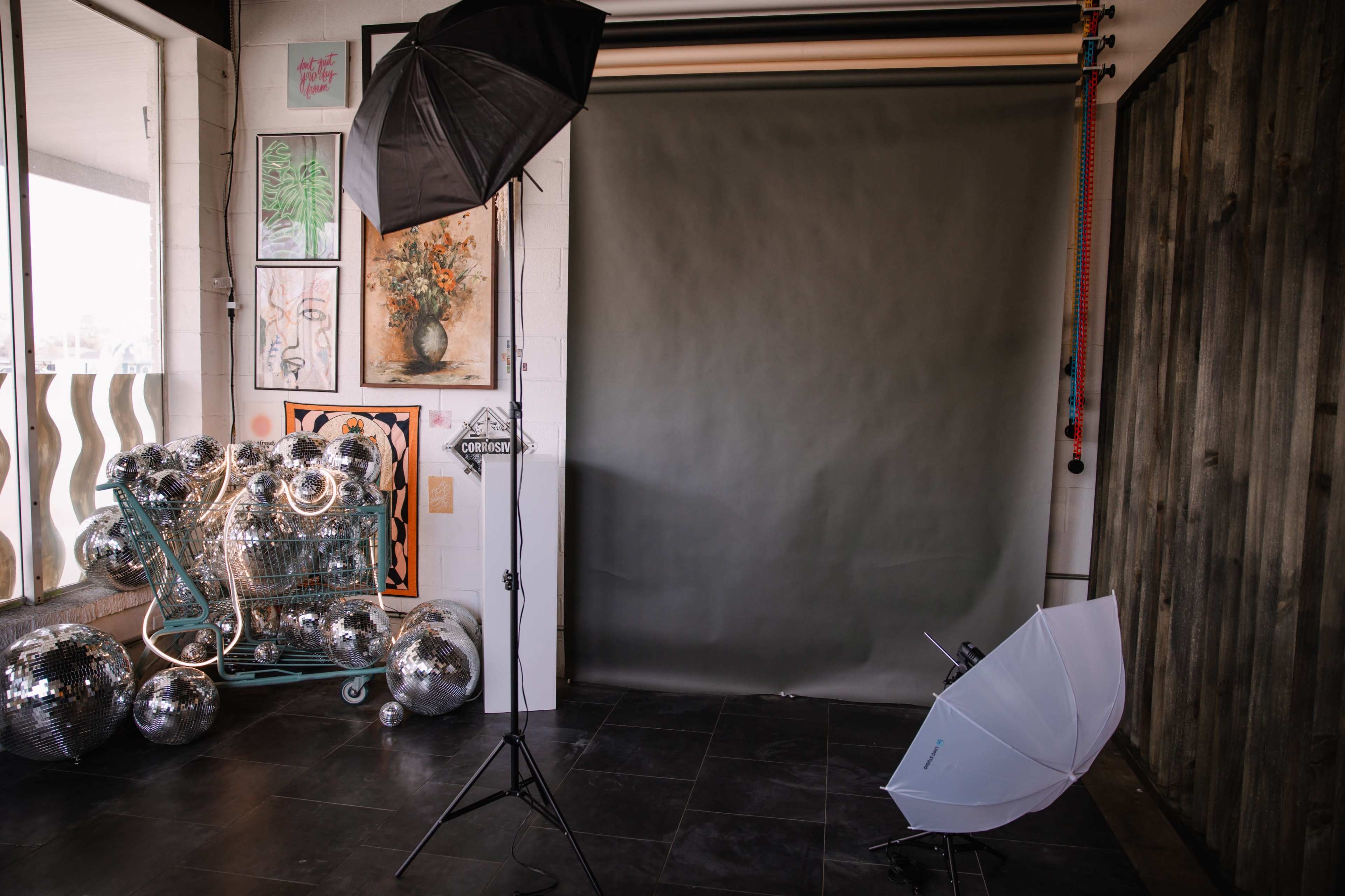 A photography studio with a gray backdrop, lighting equipment, and several disco balls piled in a cart.
