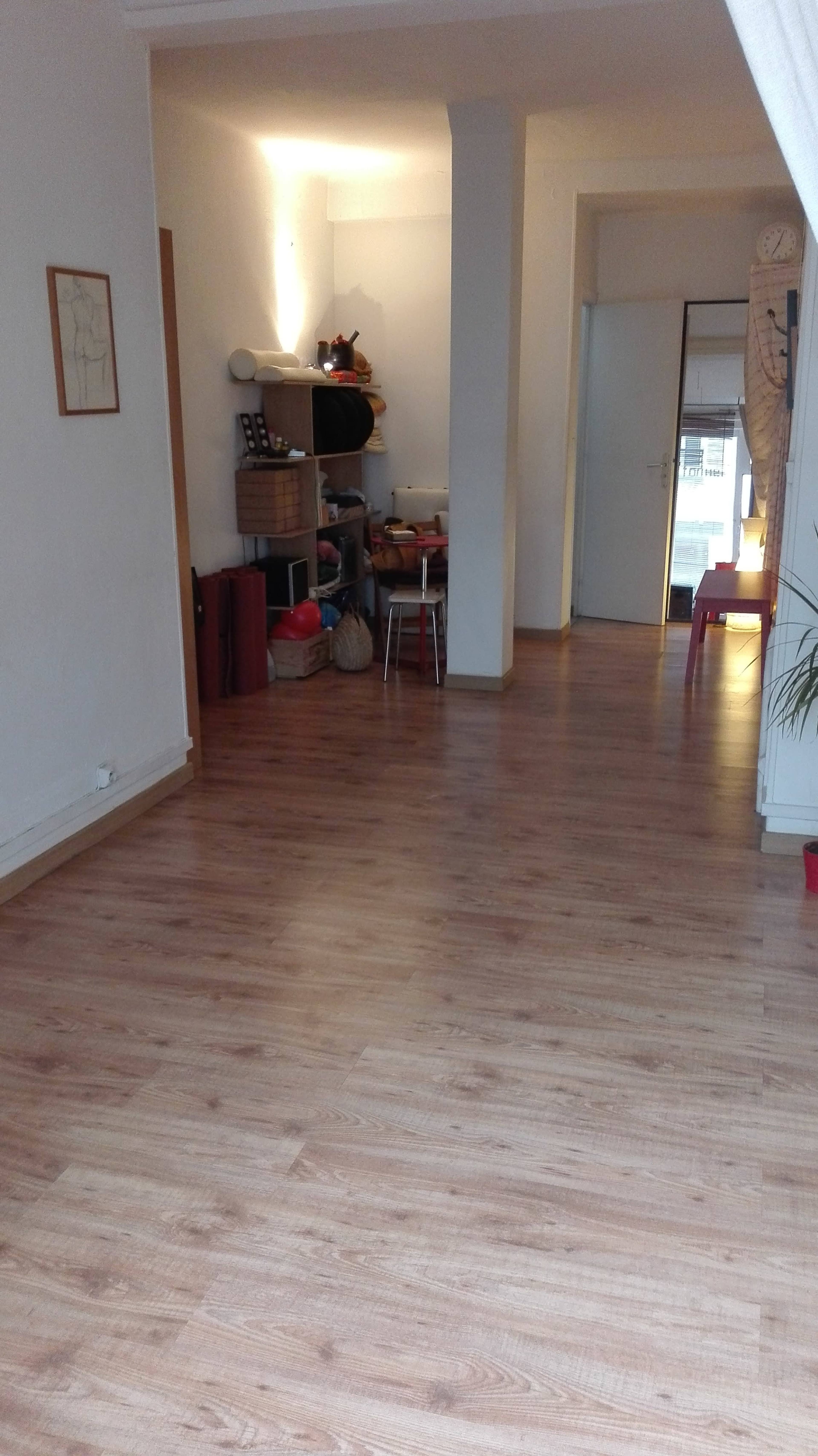 A spacious interior hallway with wooden flooring leading to a room with furniture and storage items visible.