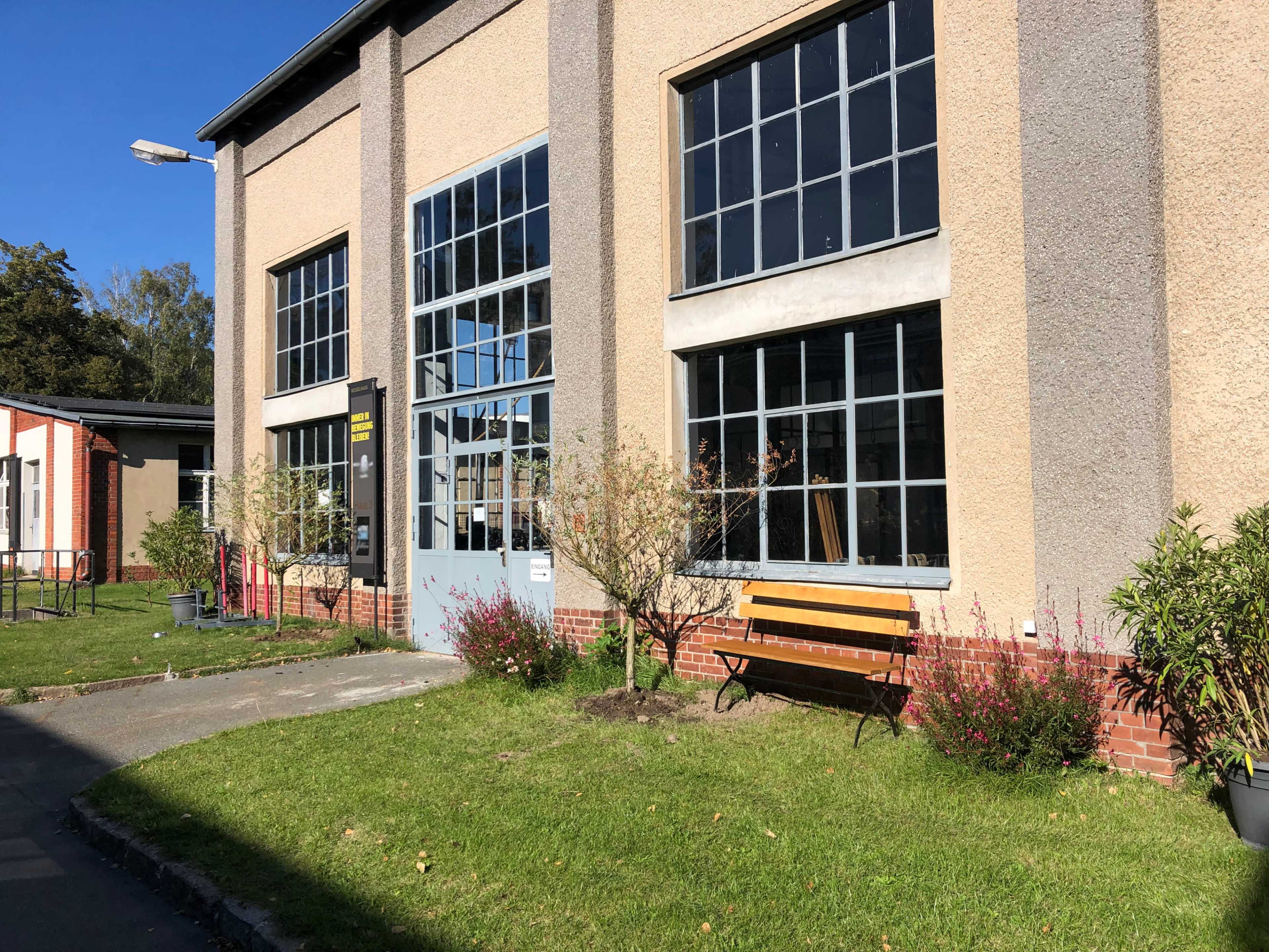 A building with large windows, a bench, and small trees in front of a grassy area.