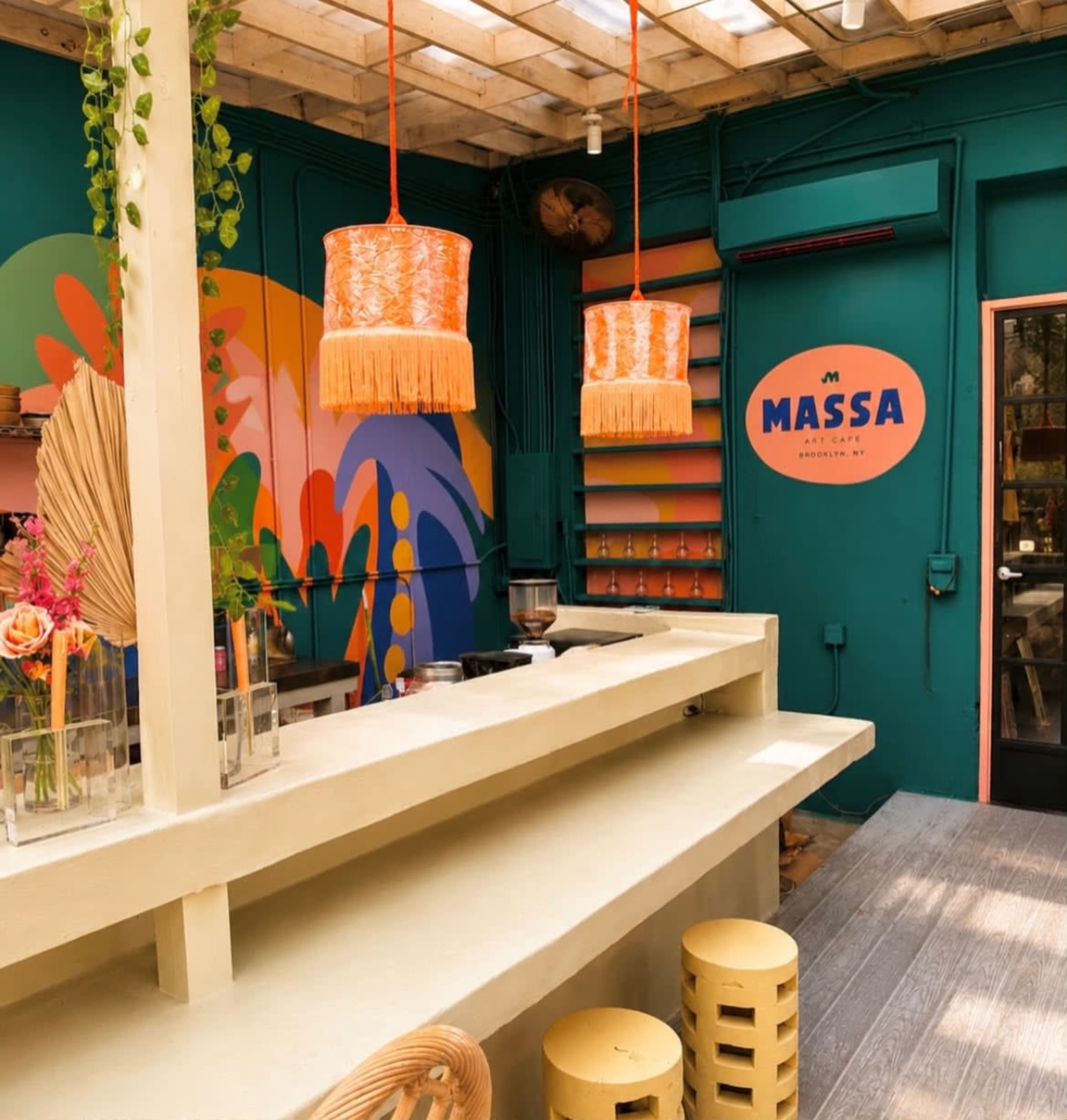 The image shows a vibrant café interior with colorful wall art, hanging light fixtures, and a counter area with decorative stools.