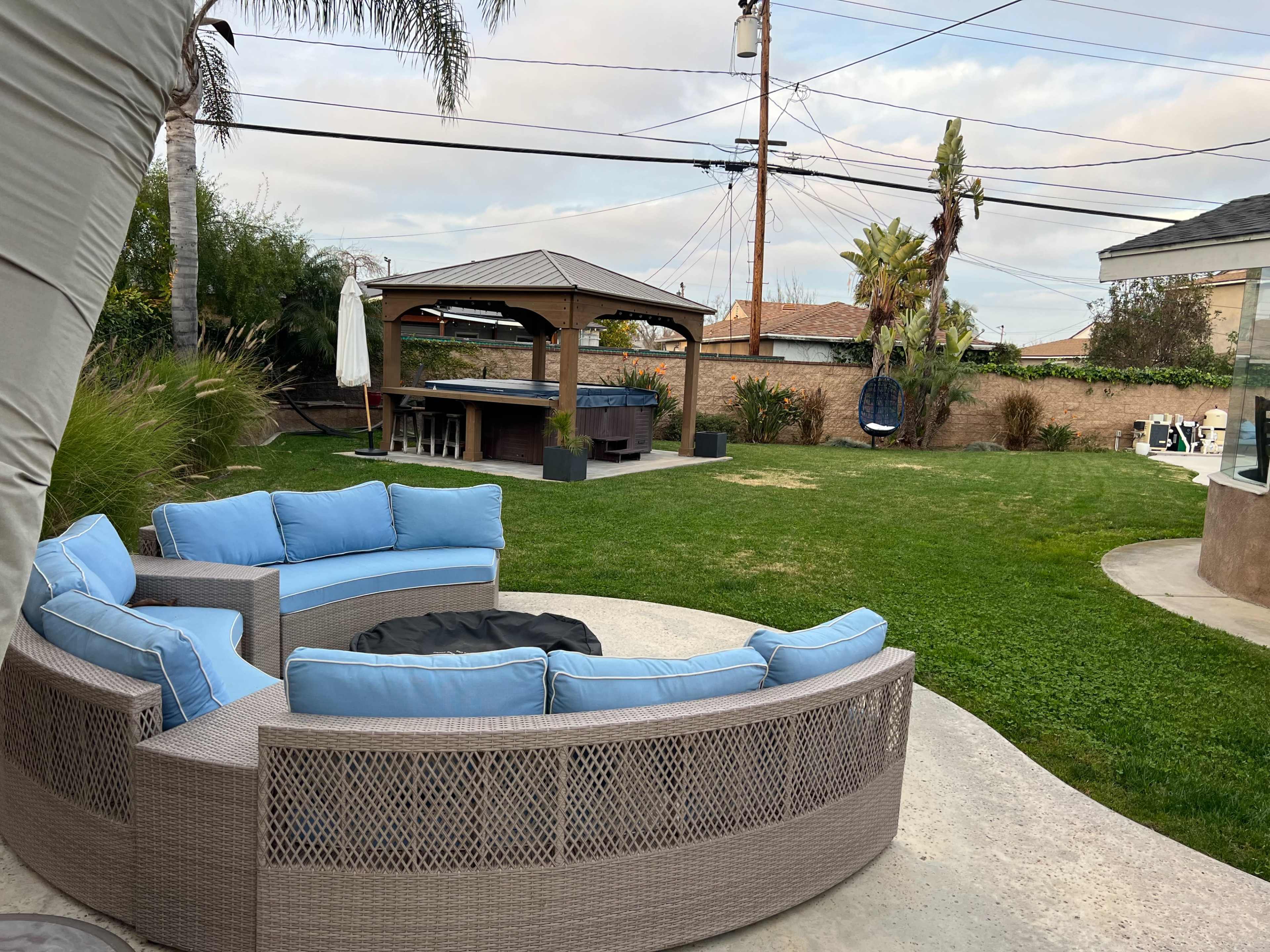 A backyard featuring a circular sectional sofa with blue cushions, a gazebo, and a well-maintained lawn with palm trees.