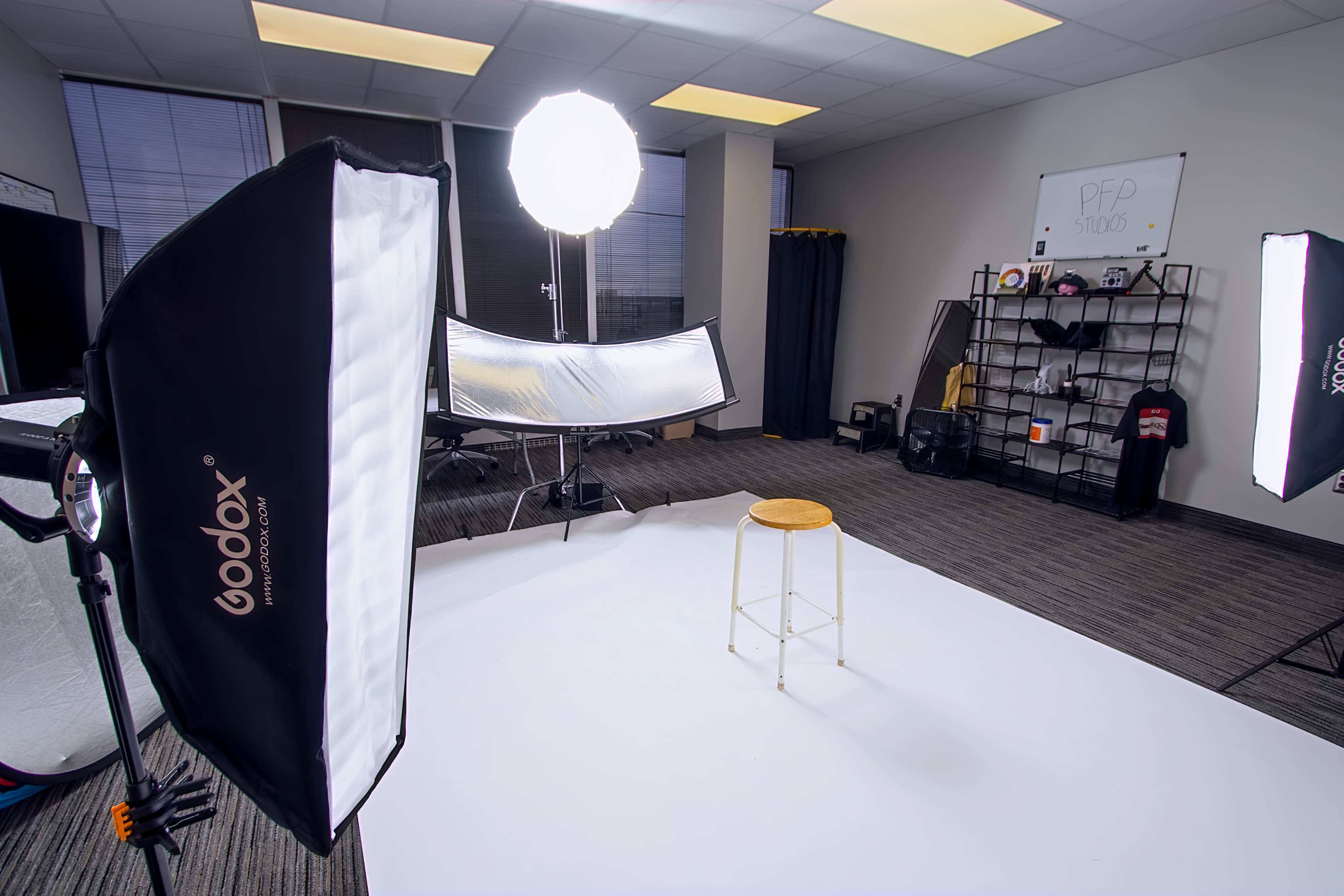 A photography studio is set up with a stool in the center, surrounded by lighting equipment and backdrops.