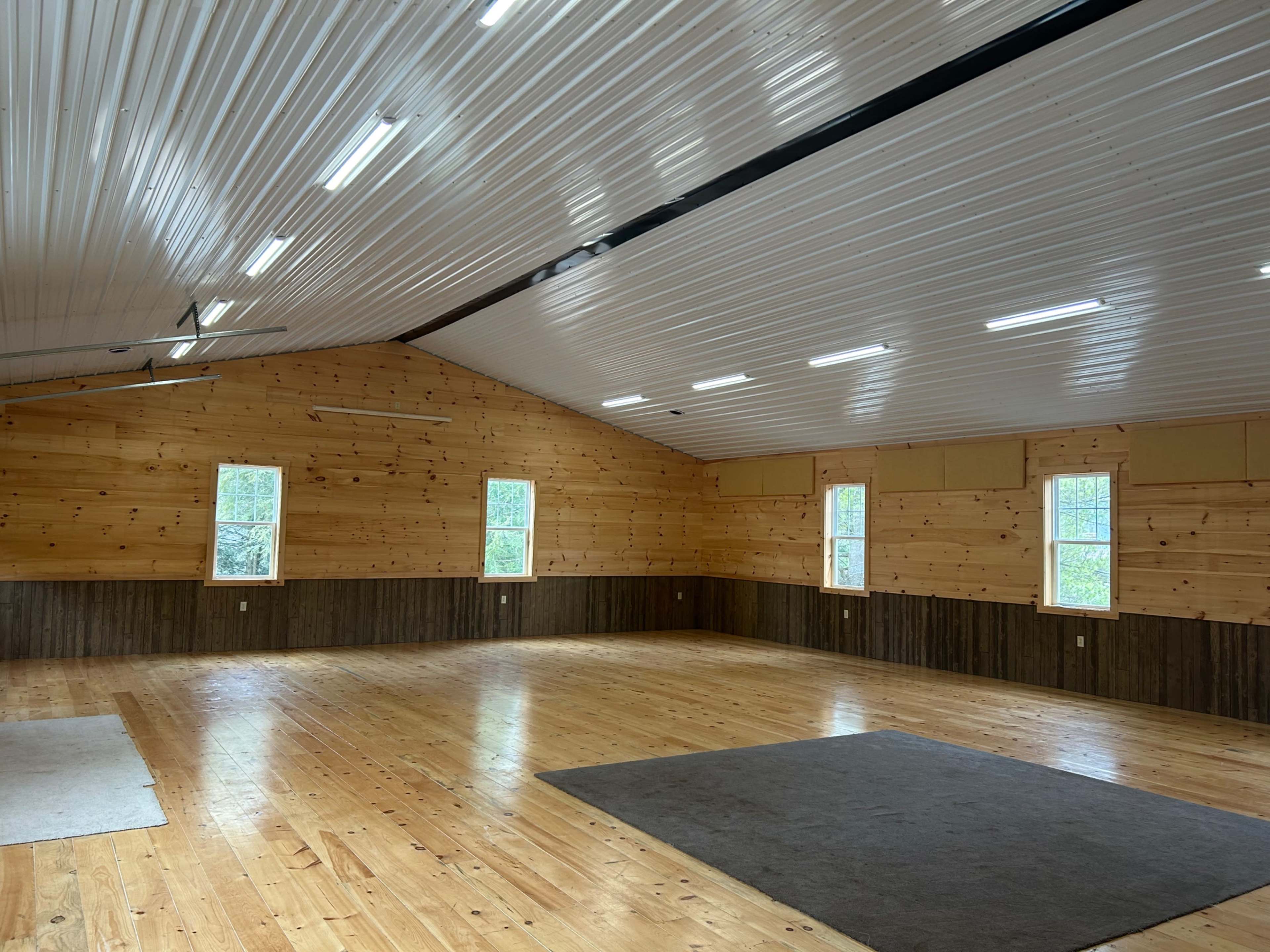 A spacious indoor room with wooden walls, a high ceiling, and several windows allowing natural light to enter.