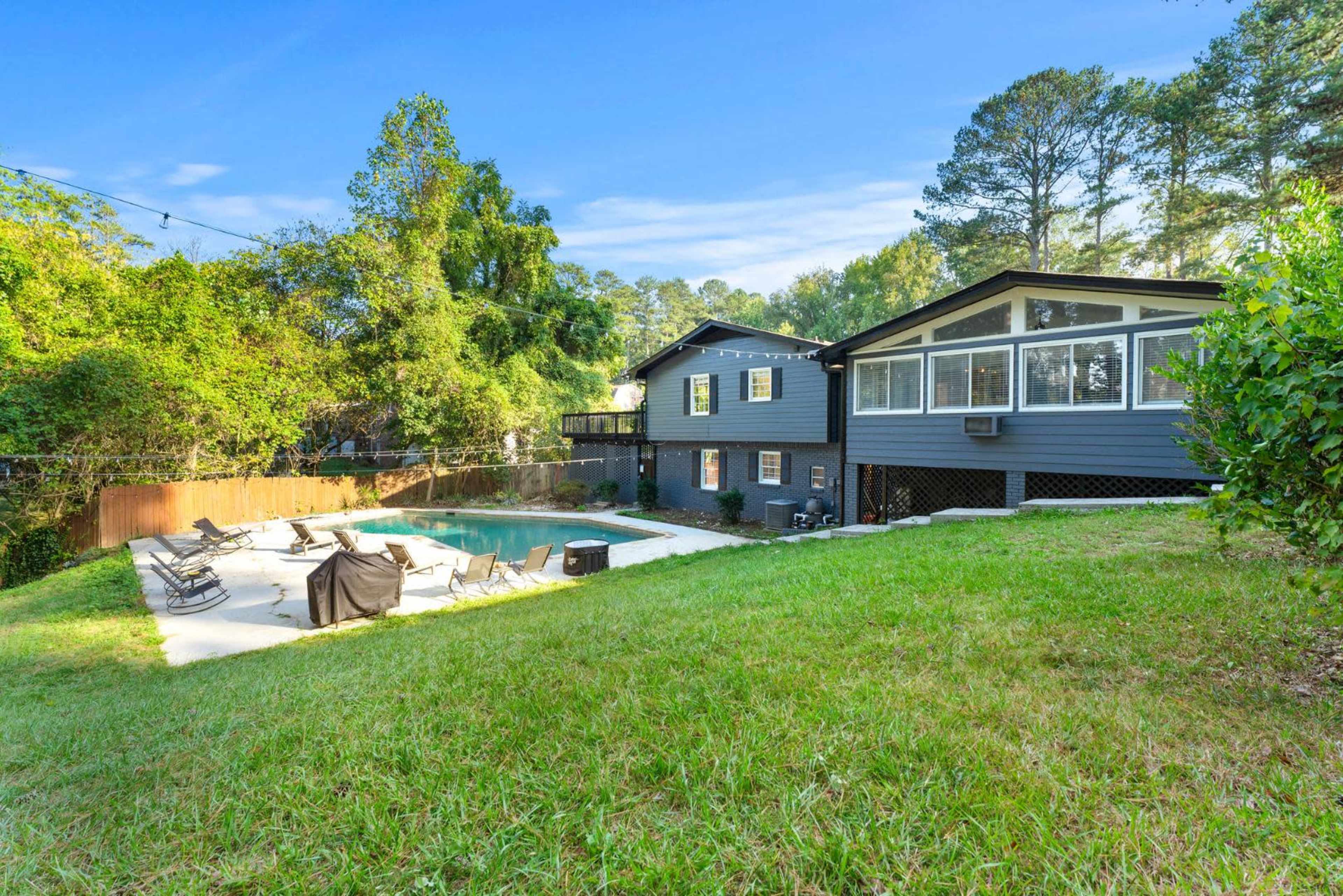 The image shows a backyard with a pool surrounded by lounge chairs, bordered by trees and a two-story house in a suburban setting.