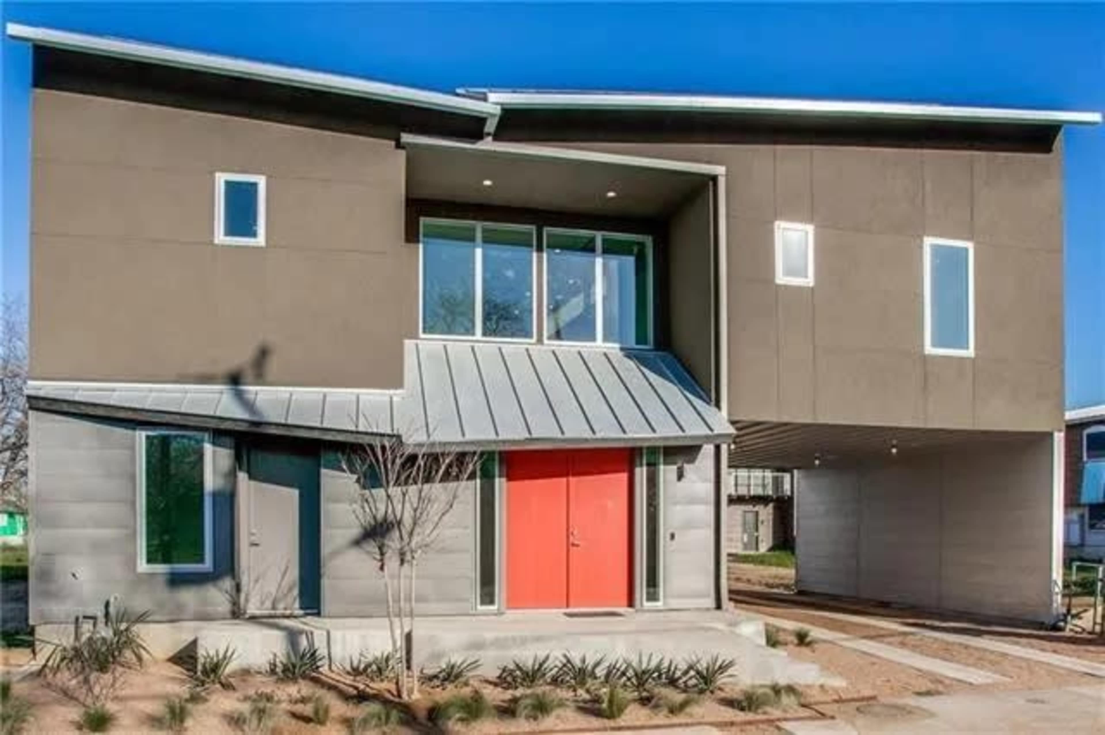 A modern two-story house features a unique angular design with a metal roof and bright red front doors.