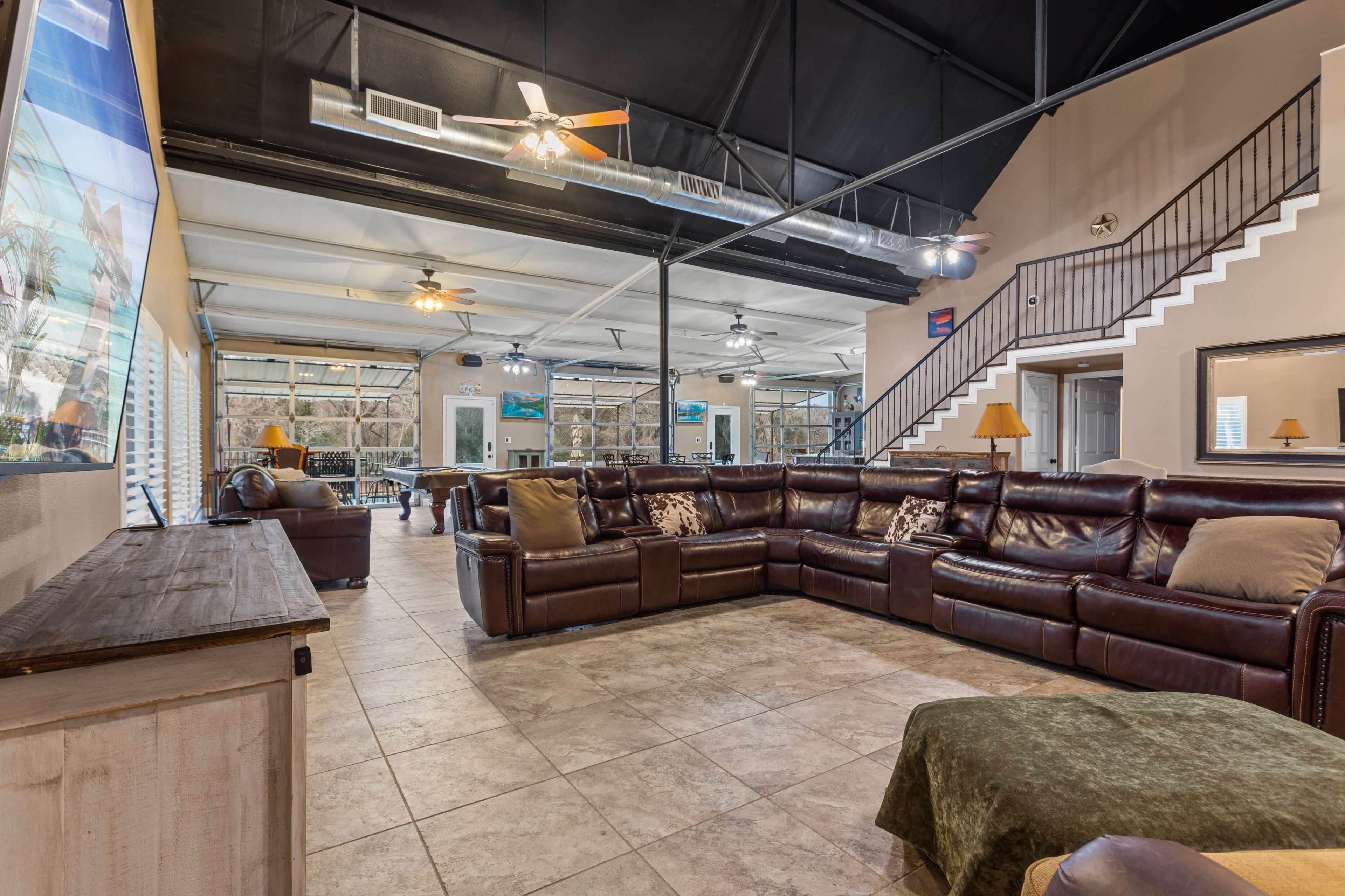 A spacious living area with a large brown sectional sofa, tiled flooring, and a staircase leading to a second level.