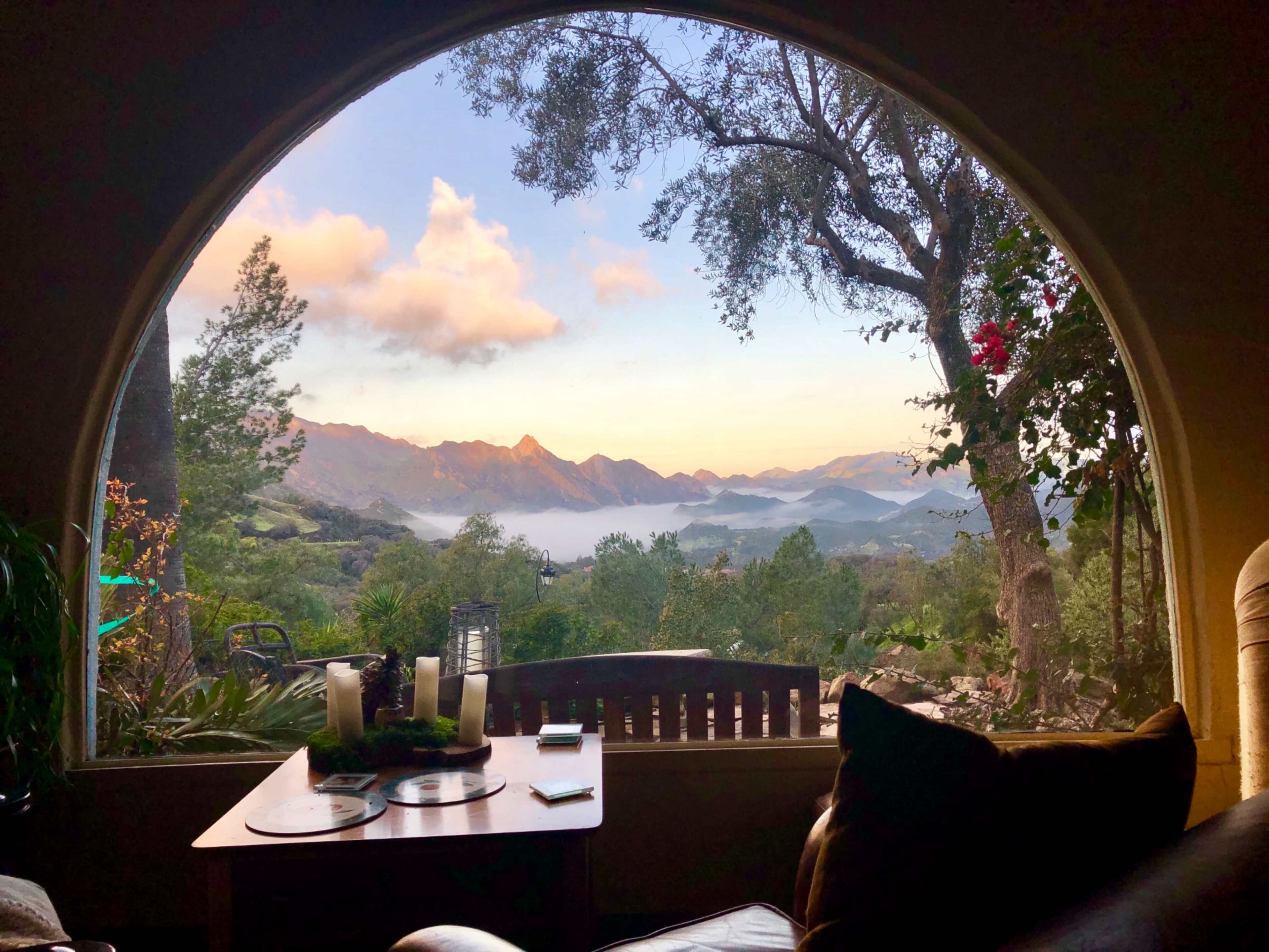 A large arched window frames a view of mountains and trees under a colorful sky at sunset.