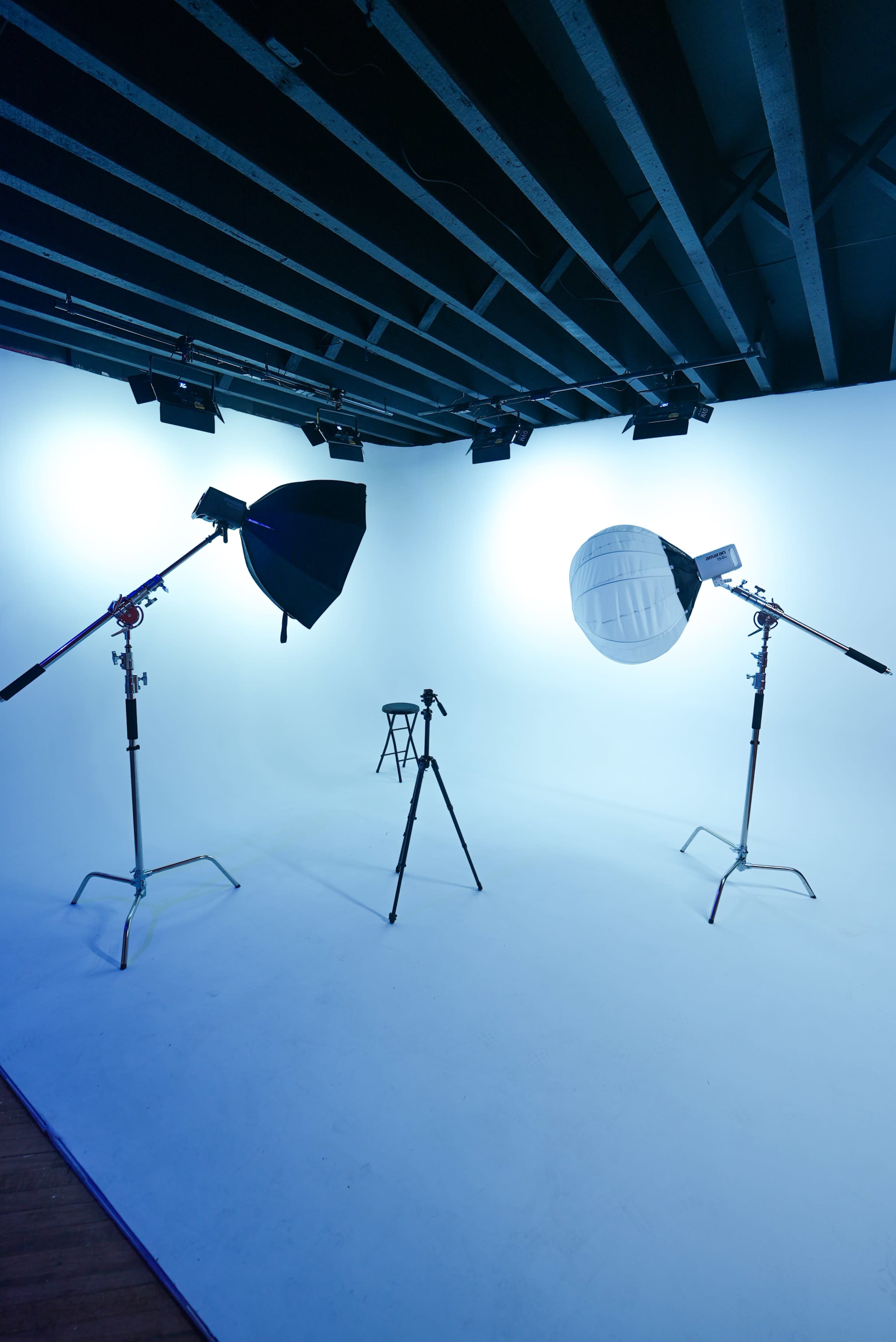 The image shows a photography studio with three lighting setups and a single stool positioned on a plain backdrop.