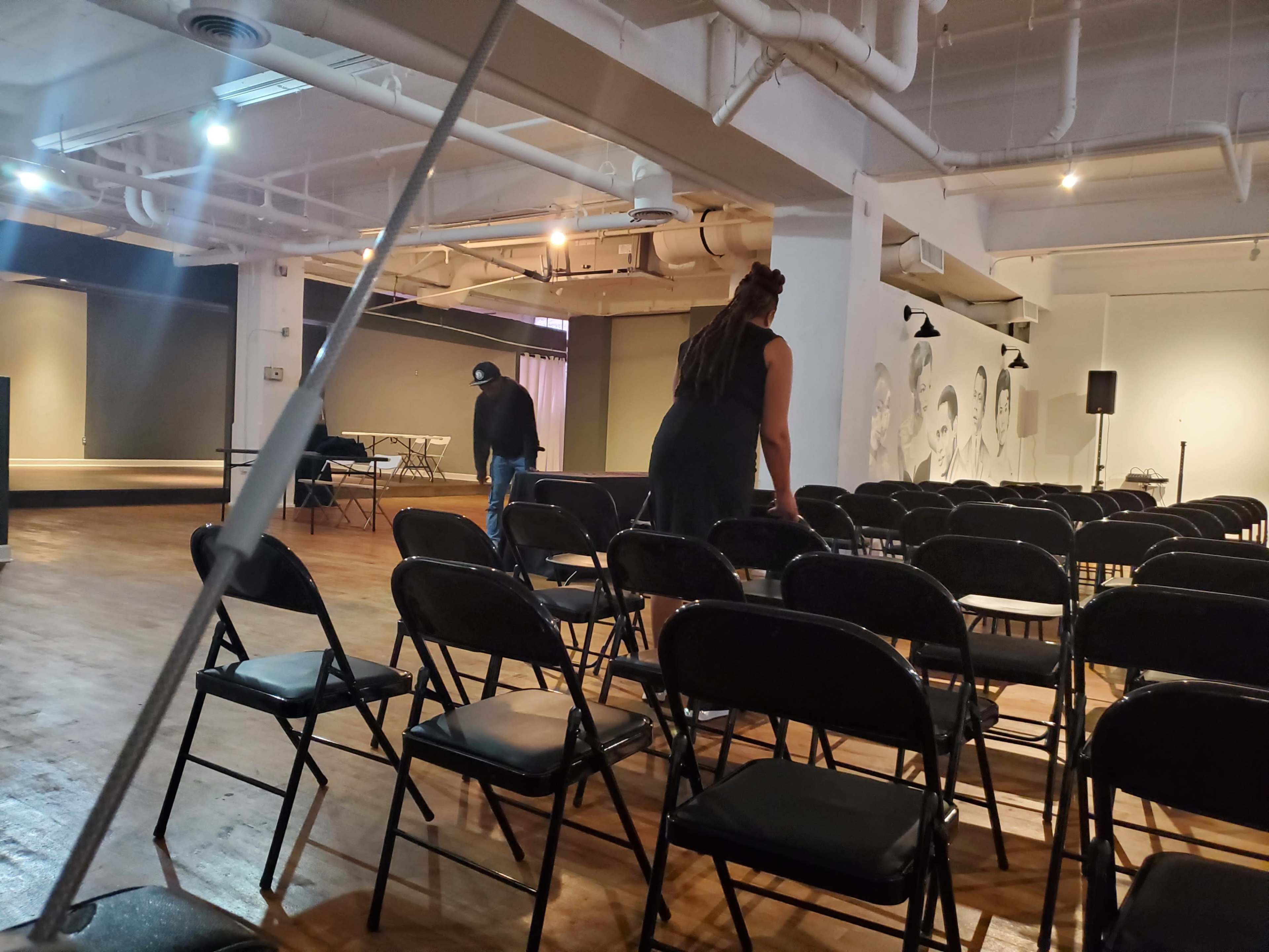 A woman adjusts folding chairs in a spacious, partially set-up venue.
