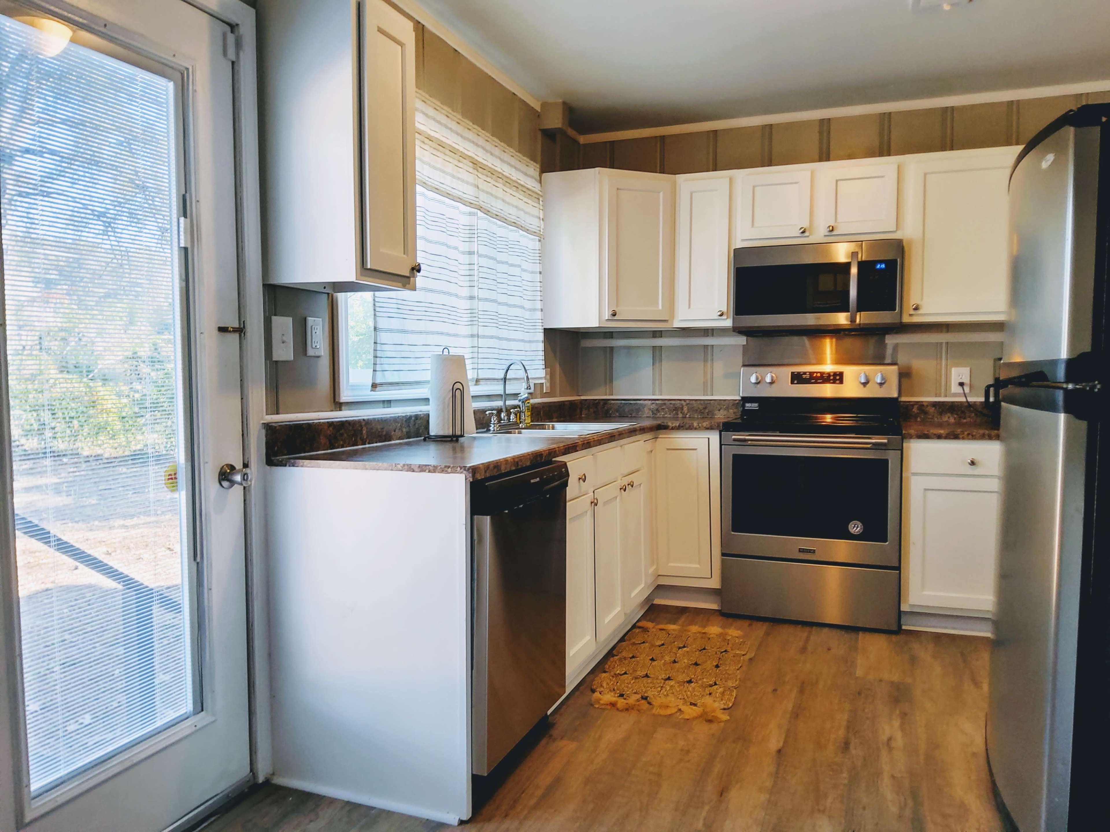 A modern kitchen features white cabinets, stainless steel appliances, and a door leading to the outside.
