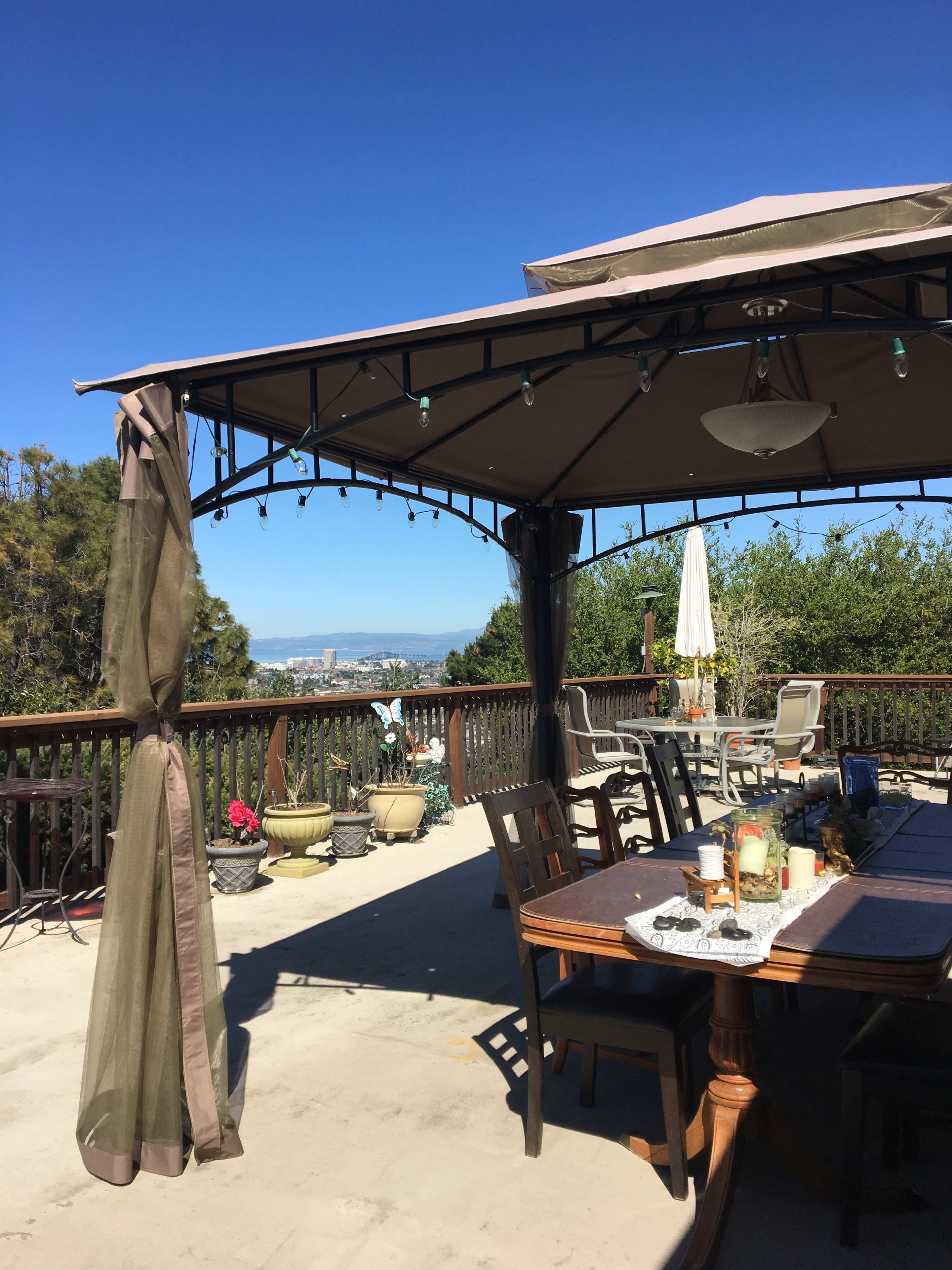 A covered outdoor seating area with a table and chairs overlooks a city view under a clear blue sky.