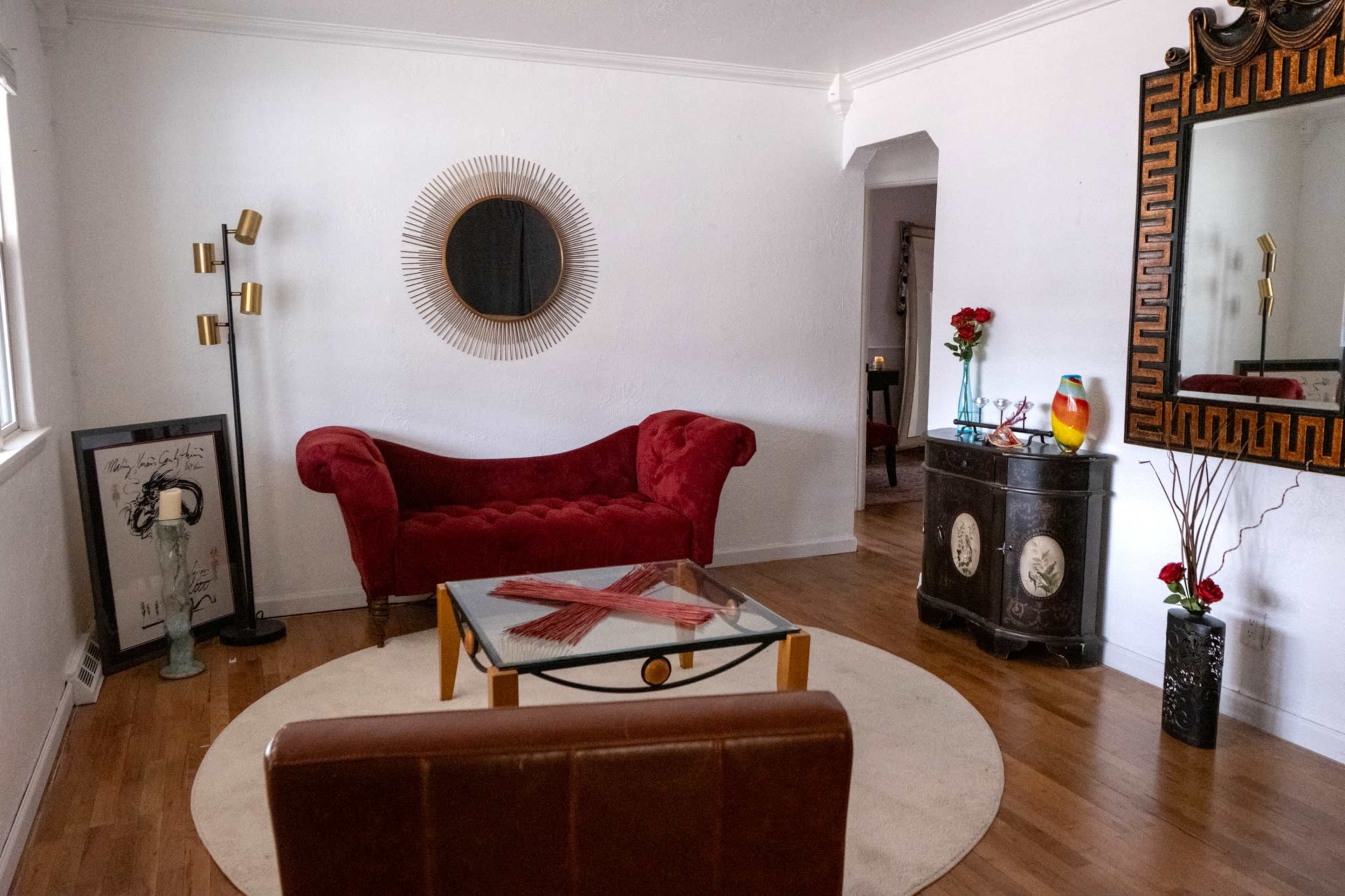 The image shows a stylish living room with a red velvet couch, a circular area rug, a glass coffee table, and a decorative mirror with an ornate frame.