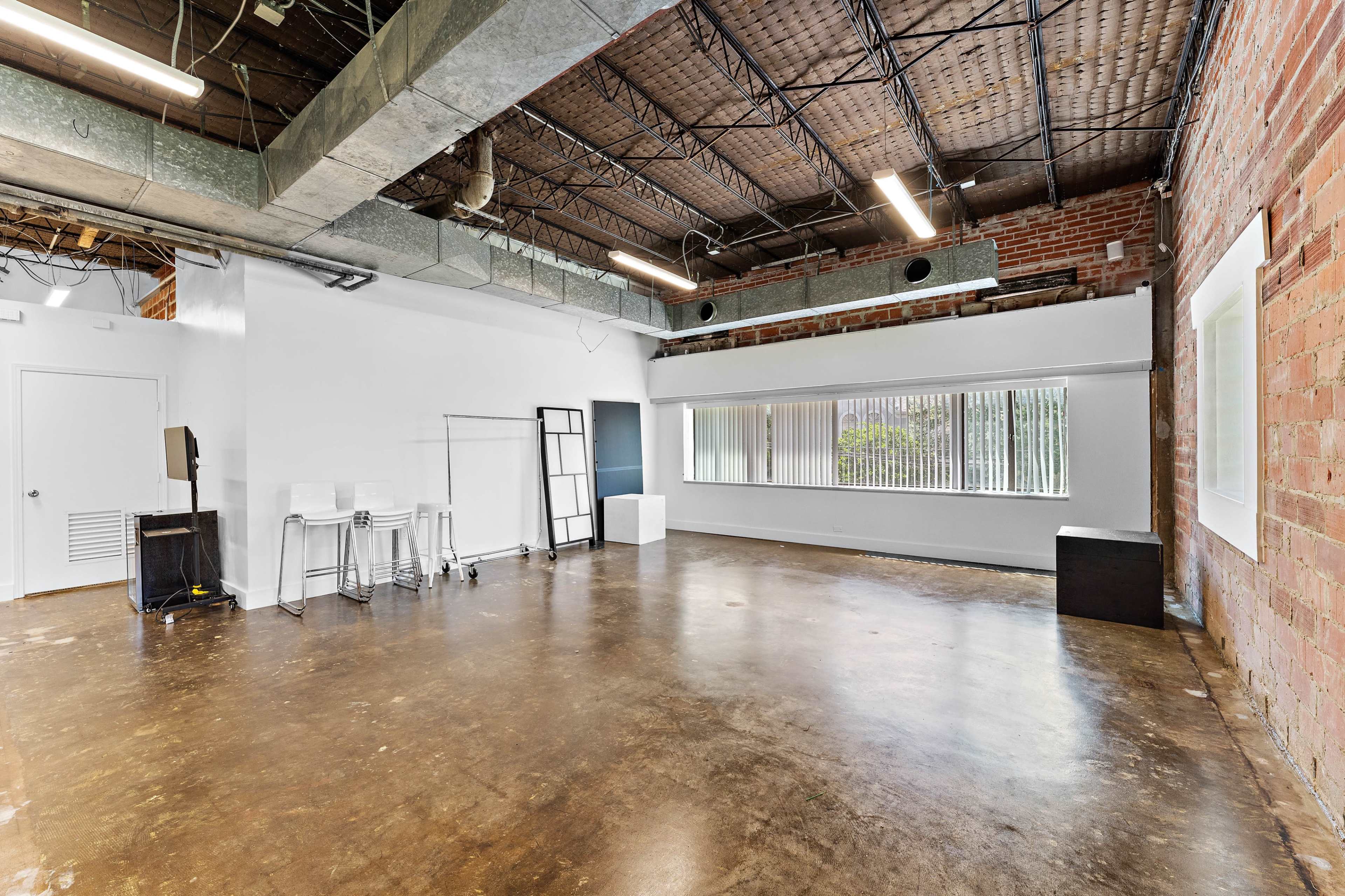 The image shows an empty room with a polished concrete floor, large windows, and exposed brick walls.