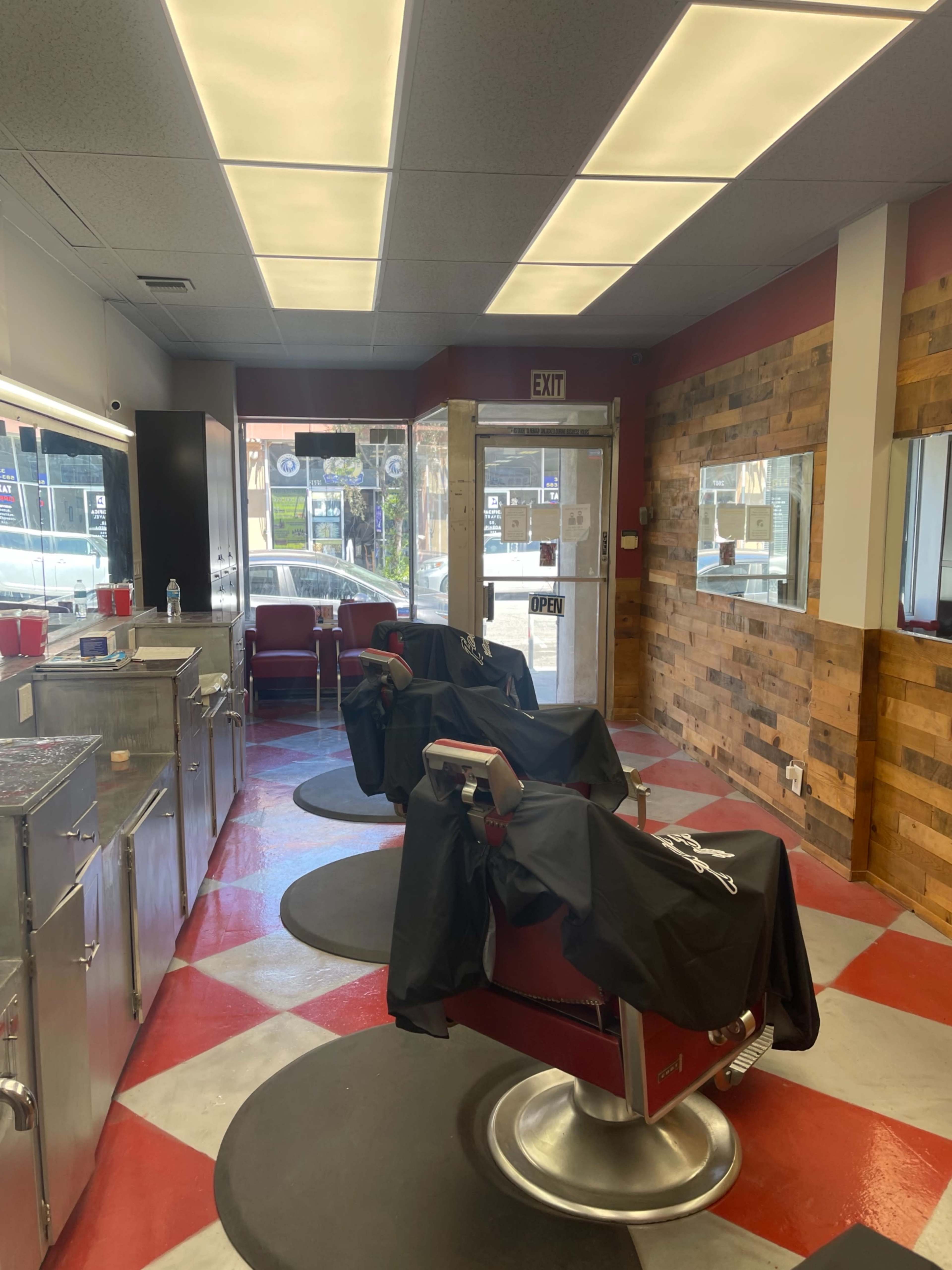 The interior of a barber shop features two barber chairs with black capes draped over them, wooden accent walls, and large mirrors.