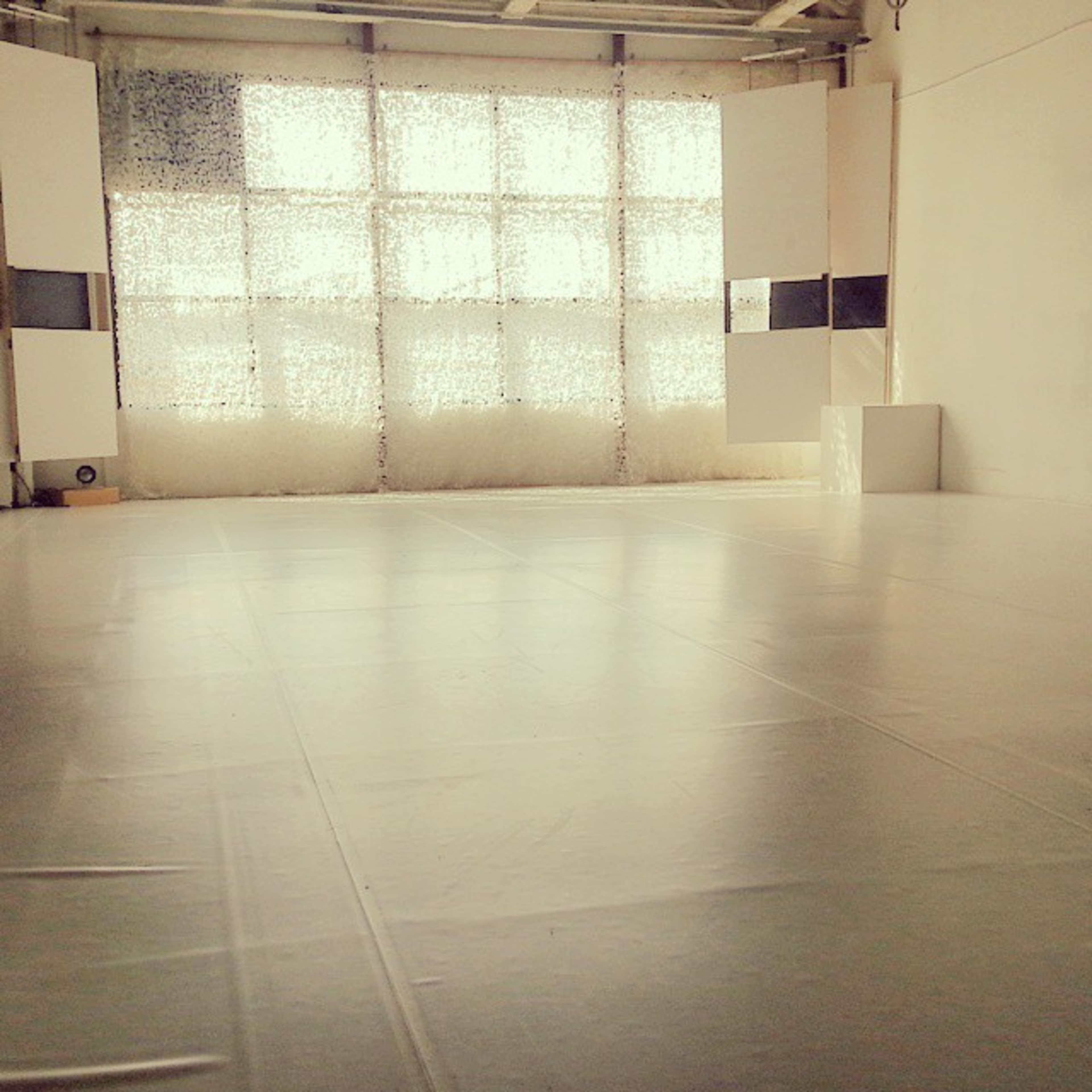 A spacious, minimalist room with a light-colored floor and large windows covered with textured panels.