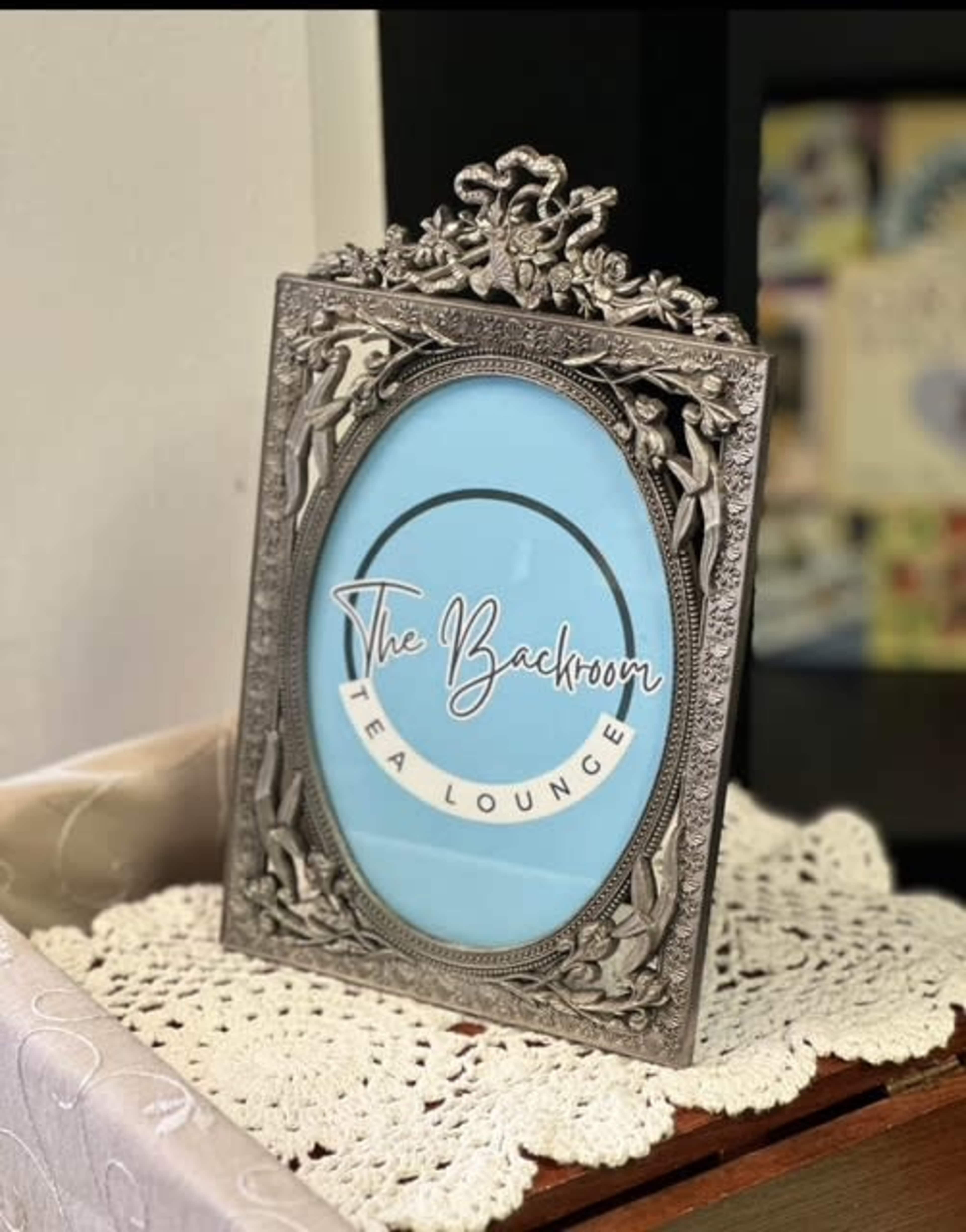 The image features a decorative silver frame displaying a sign that reads "The Backroom Tea Lounge."