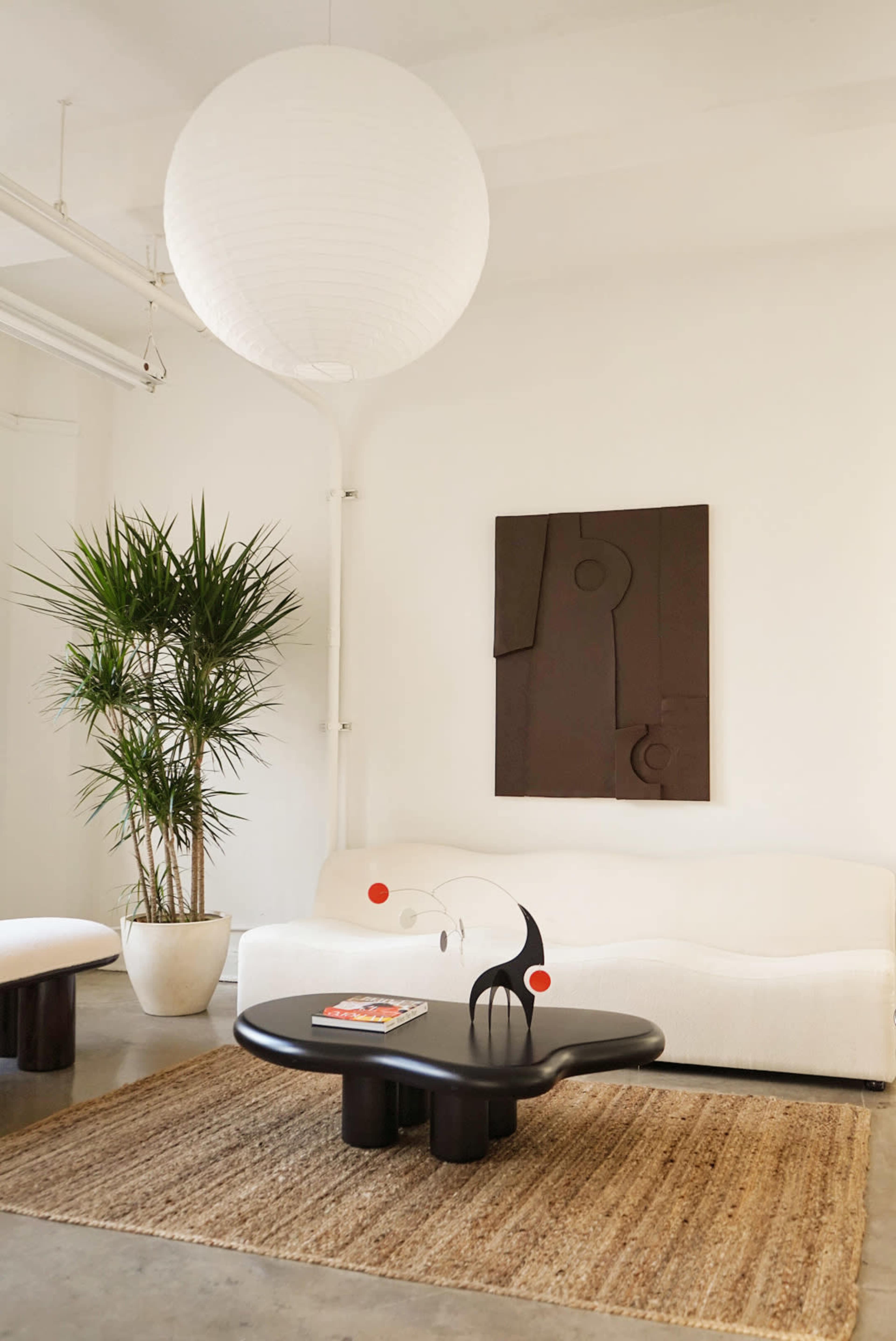 A modern living room with a white sofa, a round black coffee table, a large pendant light, and a tall plant in a pot.