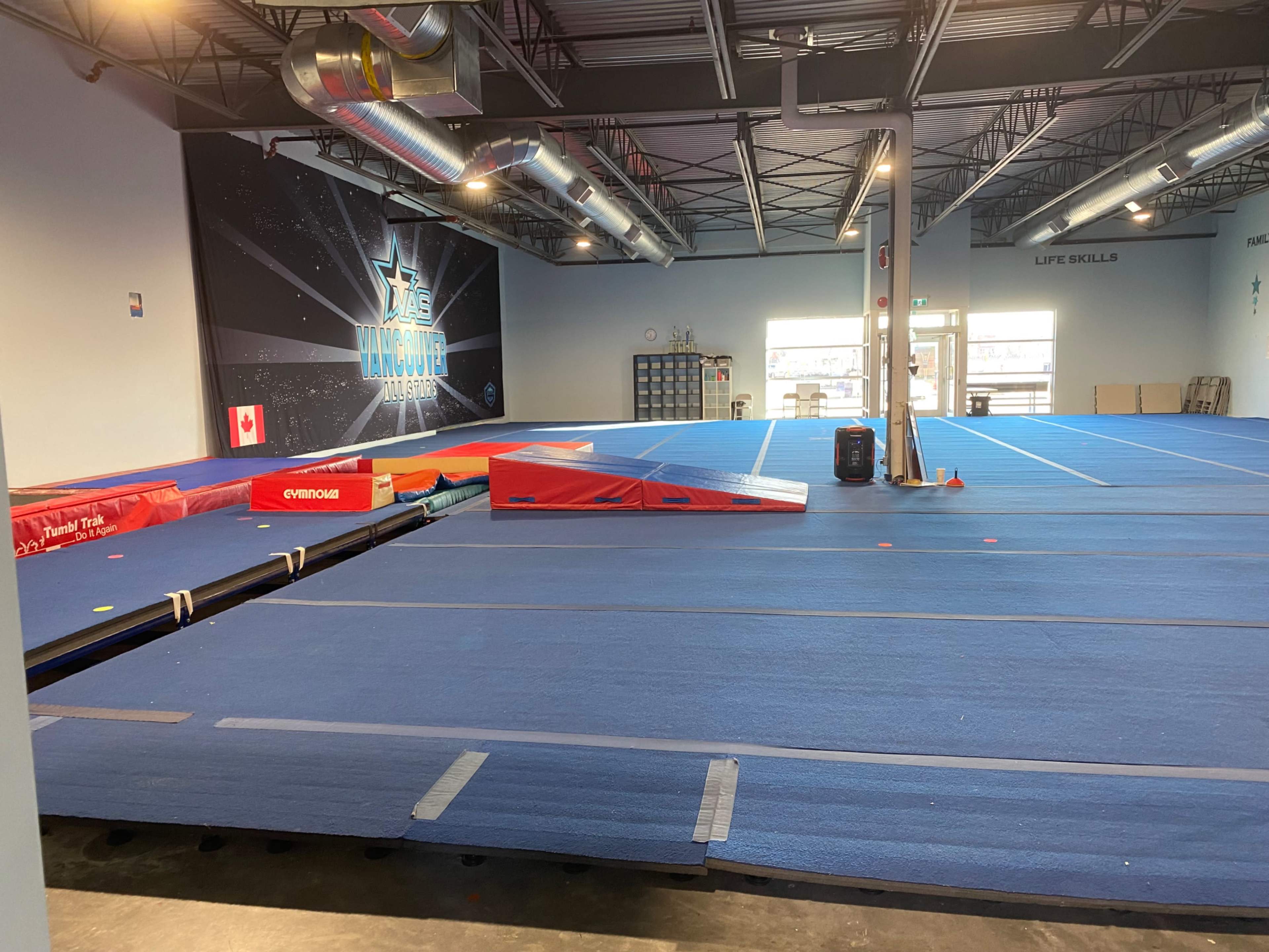 A spacious gymnastics facility featuring blue matting, various training equipment, and a large wall mural.