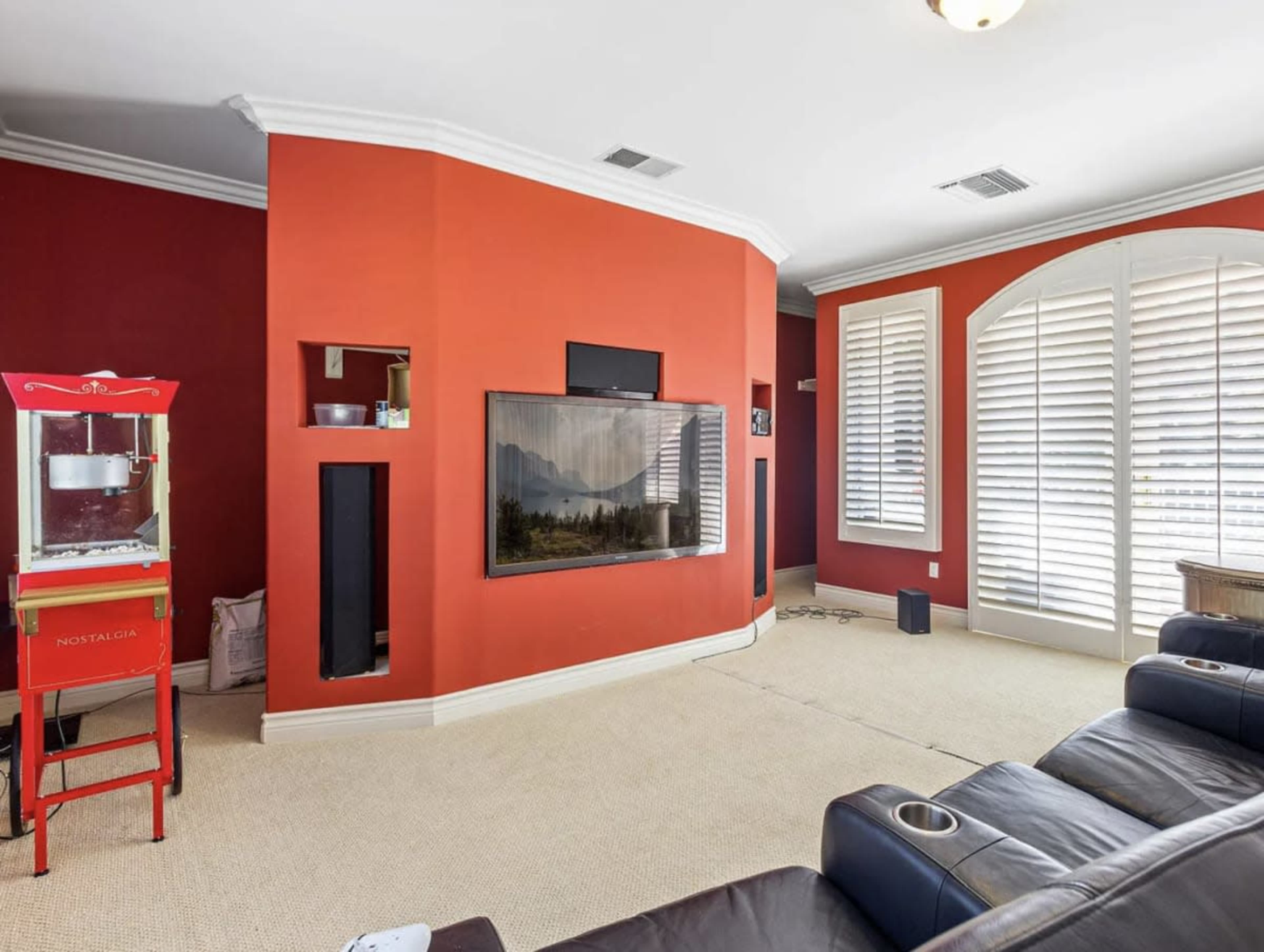 The room features a red accent wall, a mounted television, and a popcorn machine next to seating arranged for viewing.