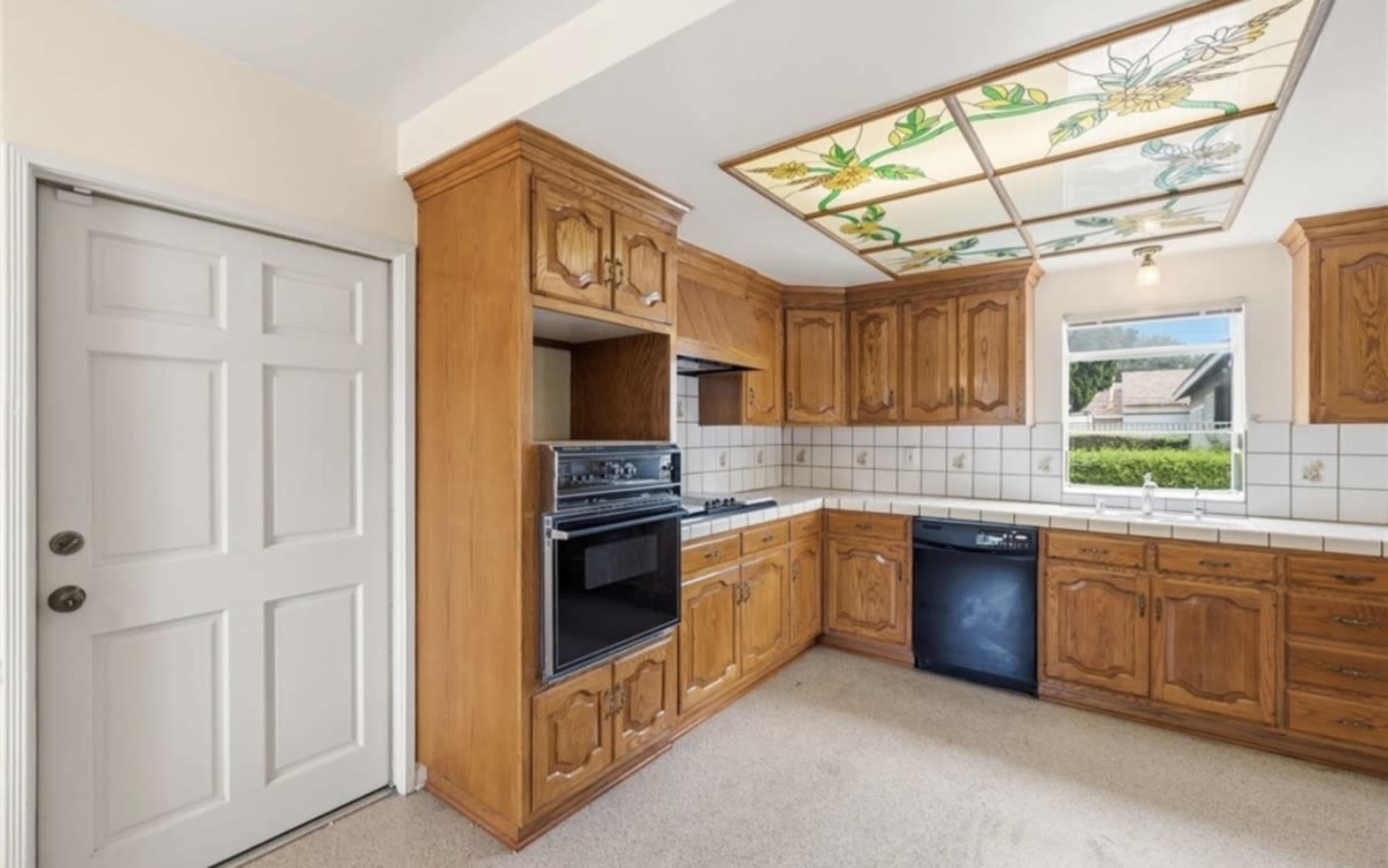The image shows a kitchen with wooden cabinetry, a tiled countertop, and a stained glass ceiling feature.