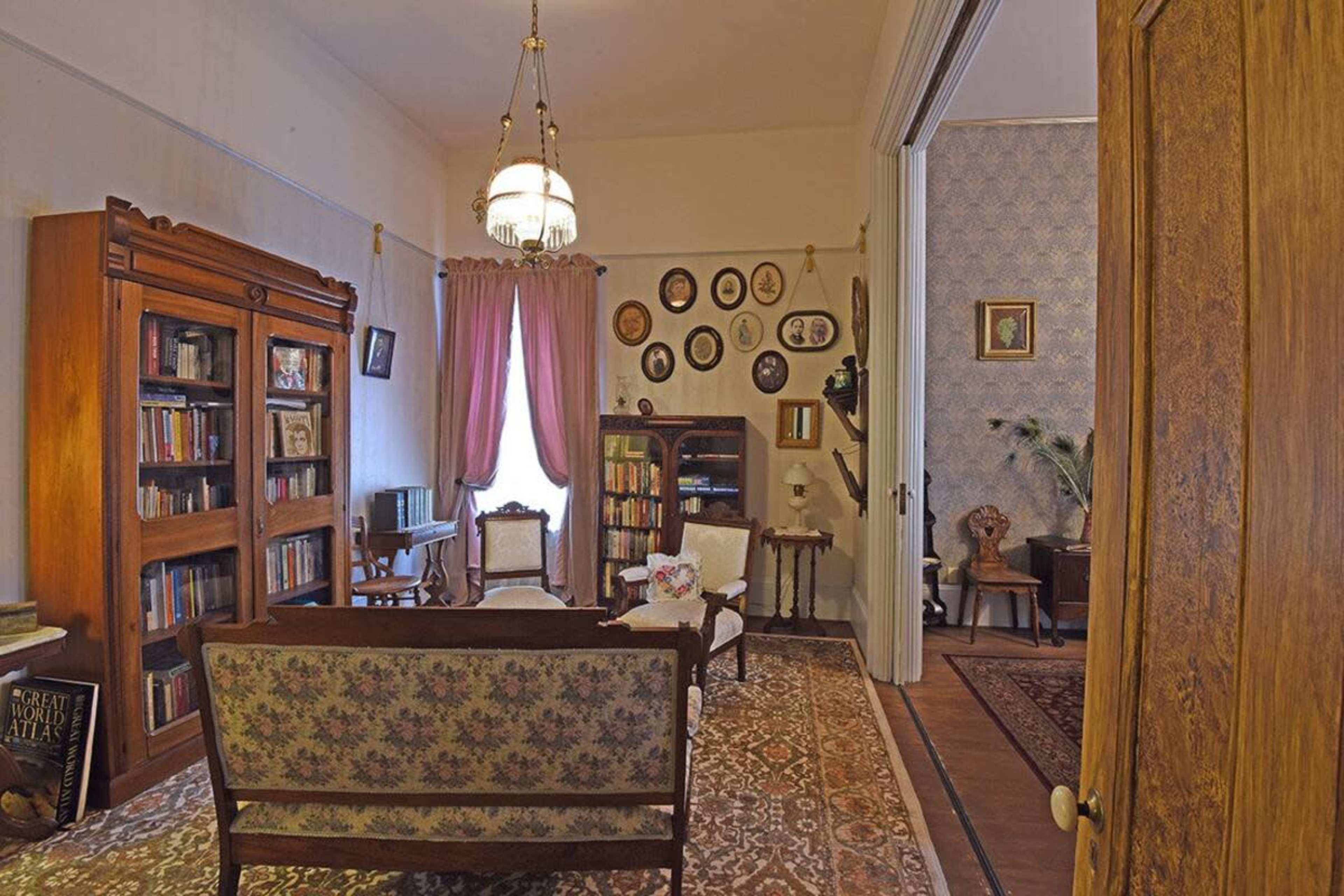 A vintage living room with a bookshelf, a floral-patterned sofa, and framed pictures hanging on the wall.