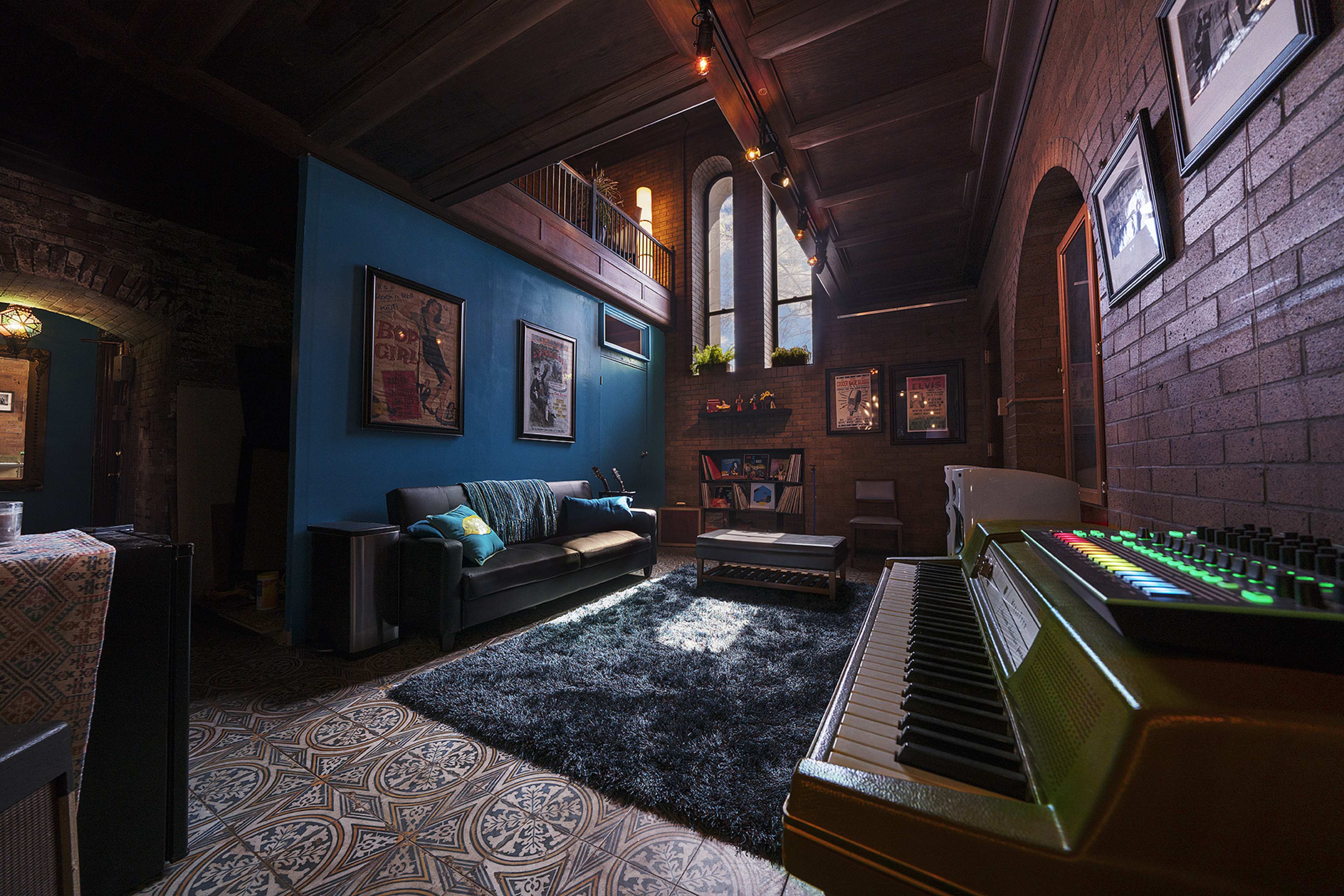 A stylish living room featuring a sofa, a coffee table on a patterned rug, and a vintage keyboard positioned in the foreground, with large windows illuminating the space.