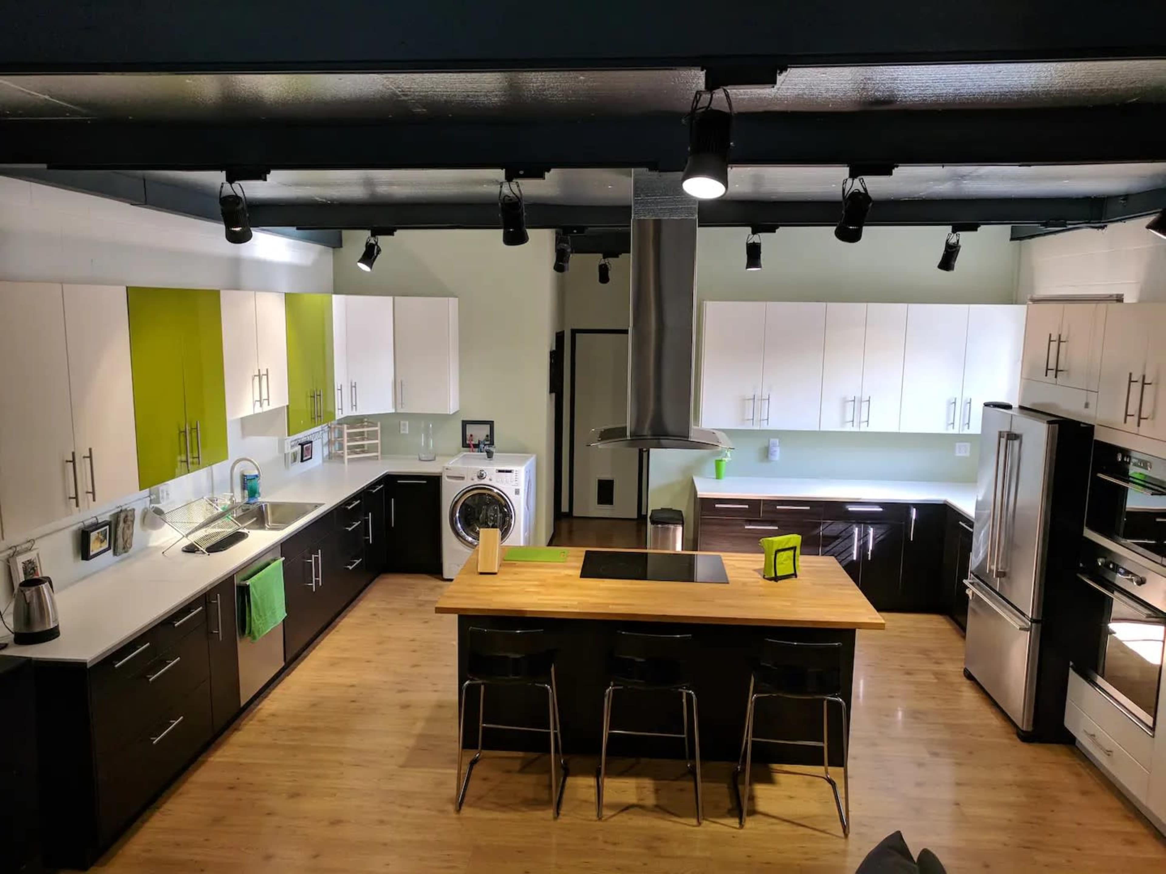 A modern kitchen featuring a central island, an array of cabinets in black, white, and green, and stainless steel appliances.