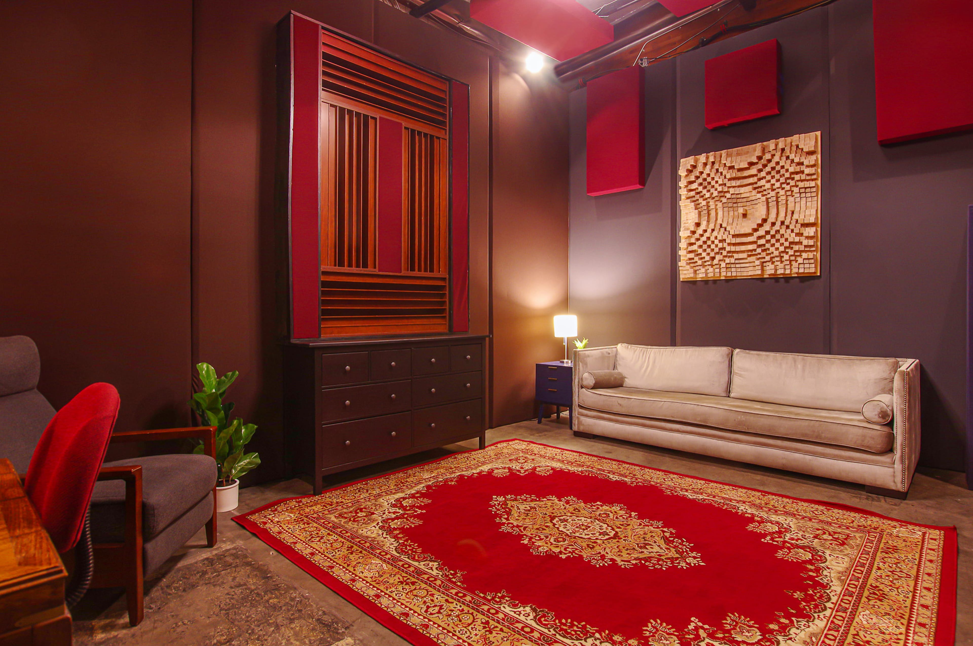 The scene features a modern room with a gray sofa, a red patterned rug, a wooden dresser, and wall art, illuminated by a small lamp.