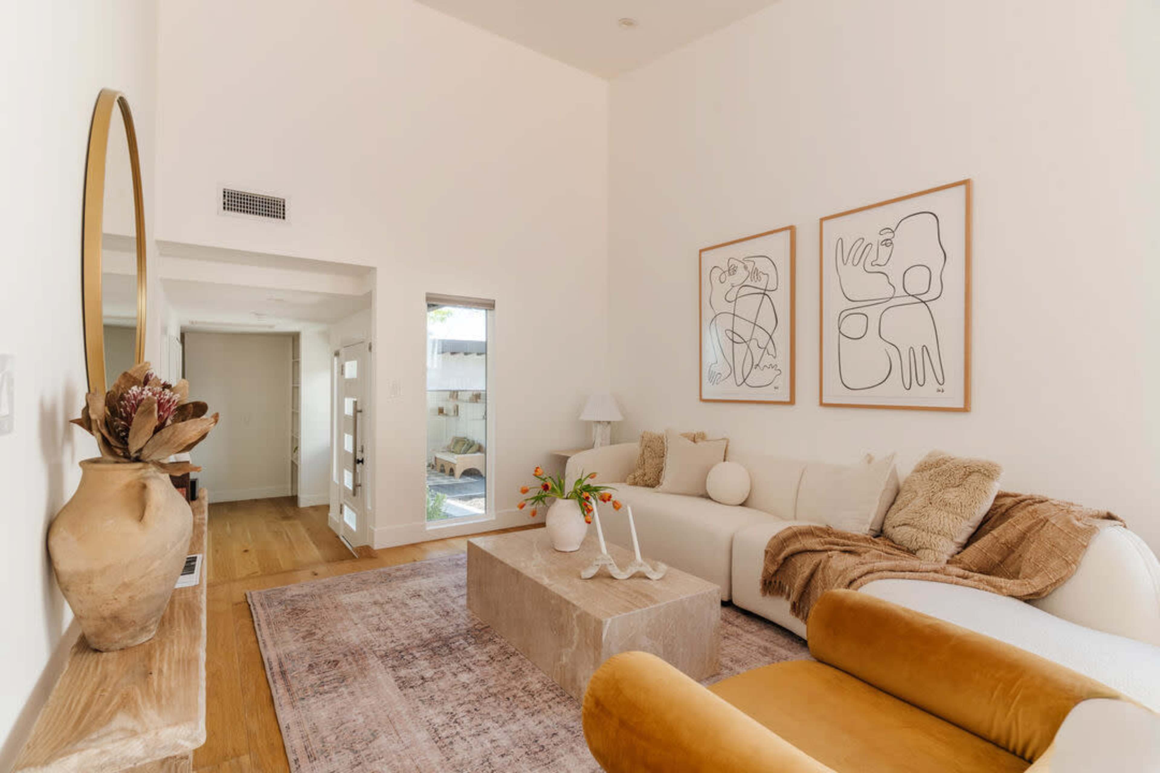 The image shows a modern living room featuring a white sofa, a wooden coffee table, and abstract artwork on the walls.