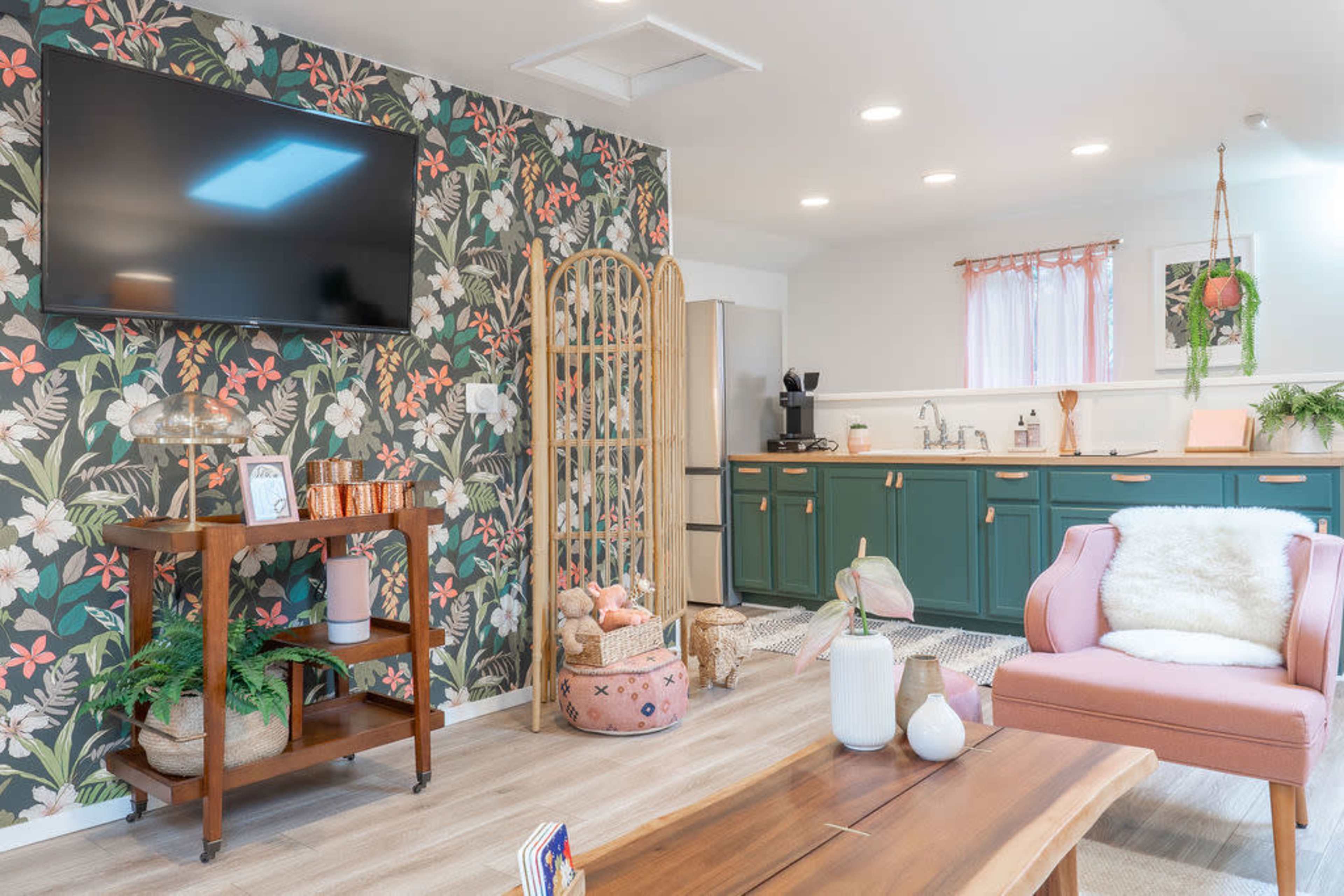 A cozy living space with floral wallpaper, a television mounted on the wall, and a kitchenette featuring green cabinetry.