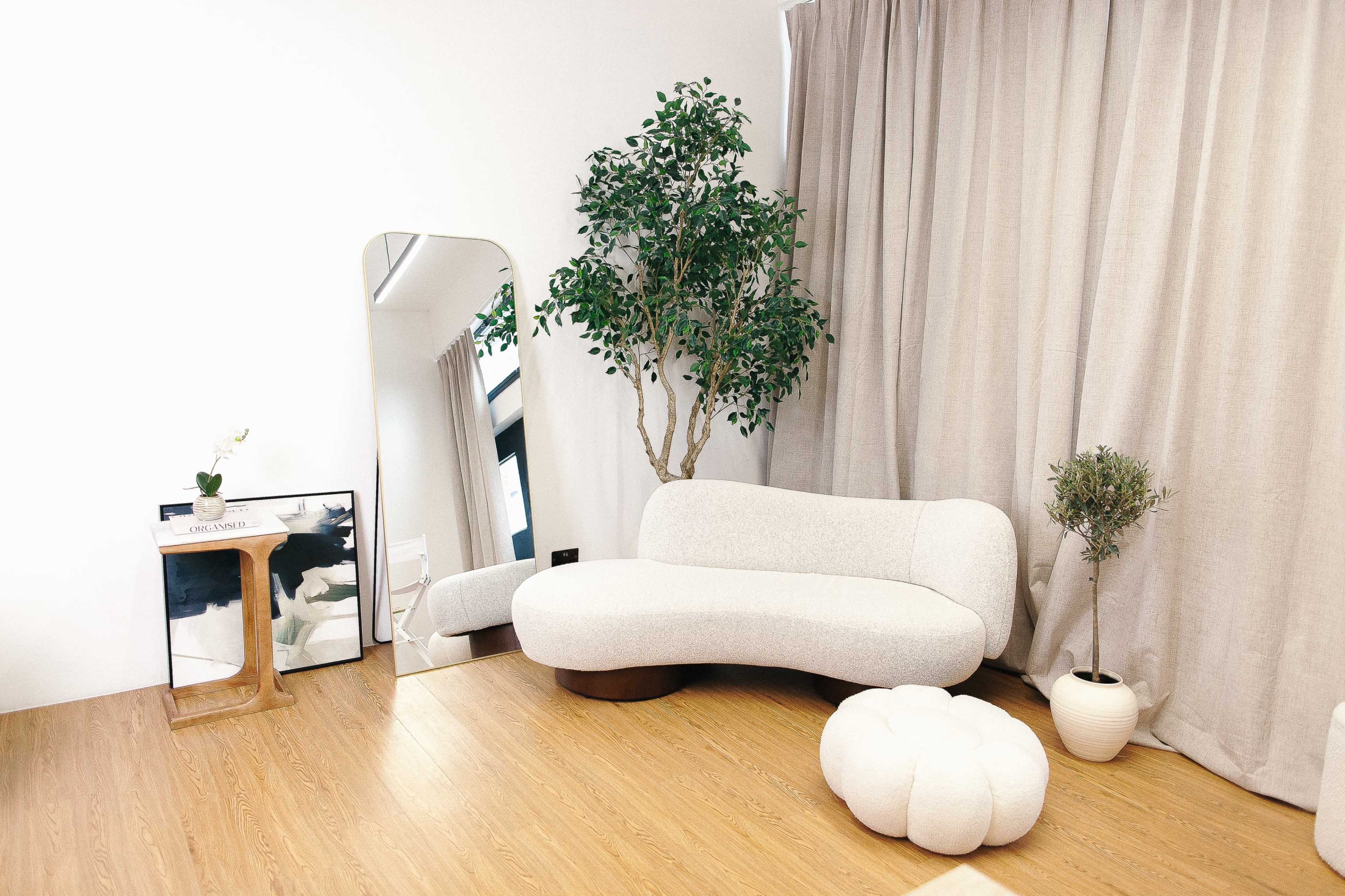 The image features a modern living room with a curved white sofa, a large mirror, a decorative plant, and a light wood floor.