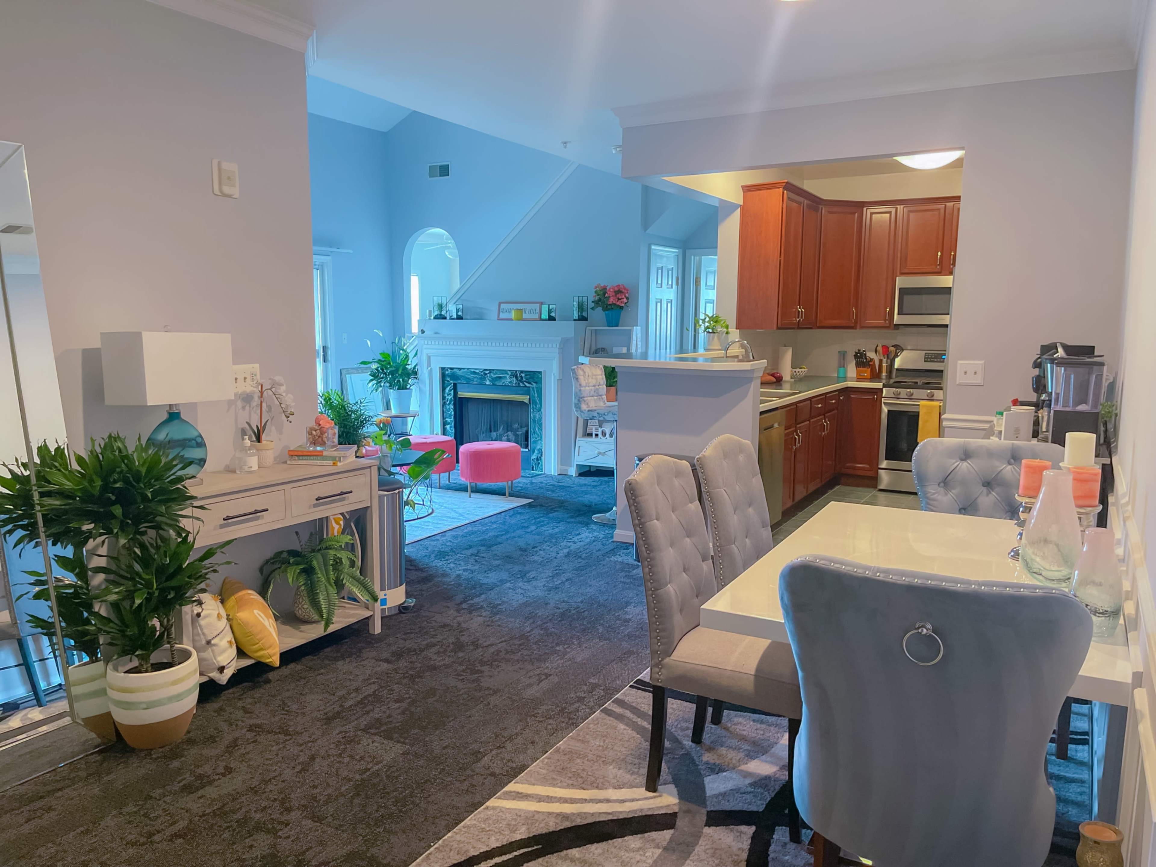 A modern open-concept living space featuring a dining area with grey chairs, a kitchen with wooden cabinets, and a lounge area with a fireplace and colorful accents.