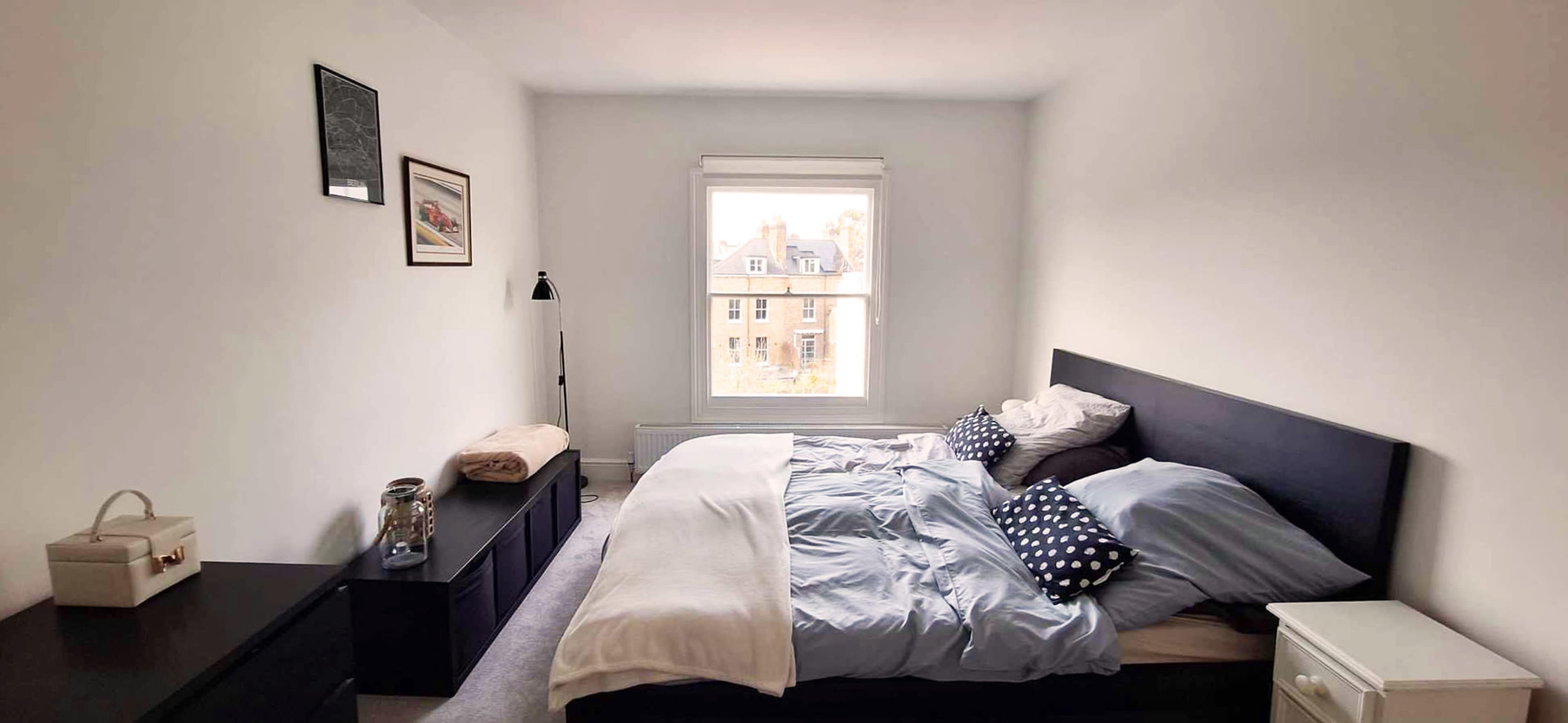 The image shows a bedroom with a neatly made bed, black furniture, and a window that lets in natural light.