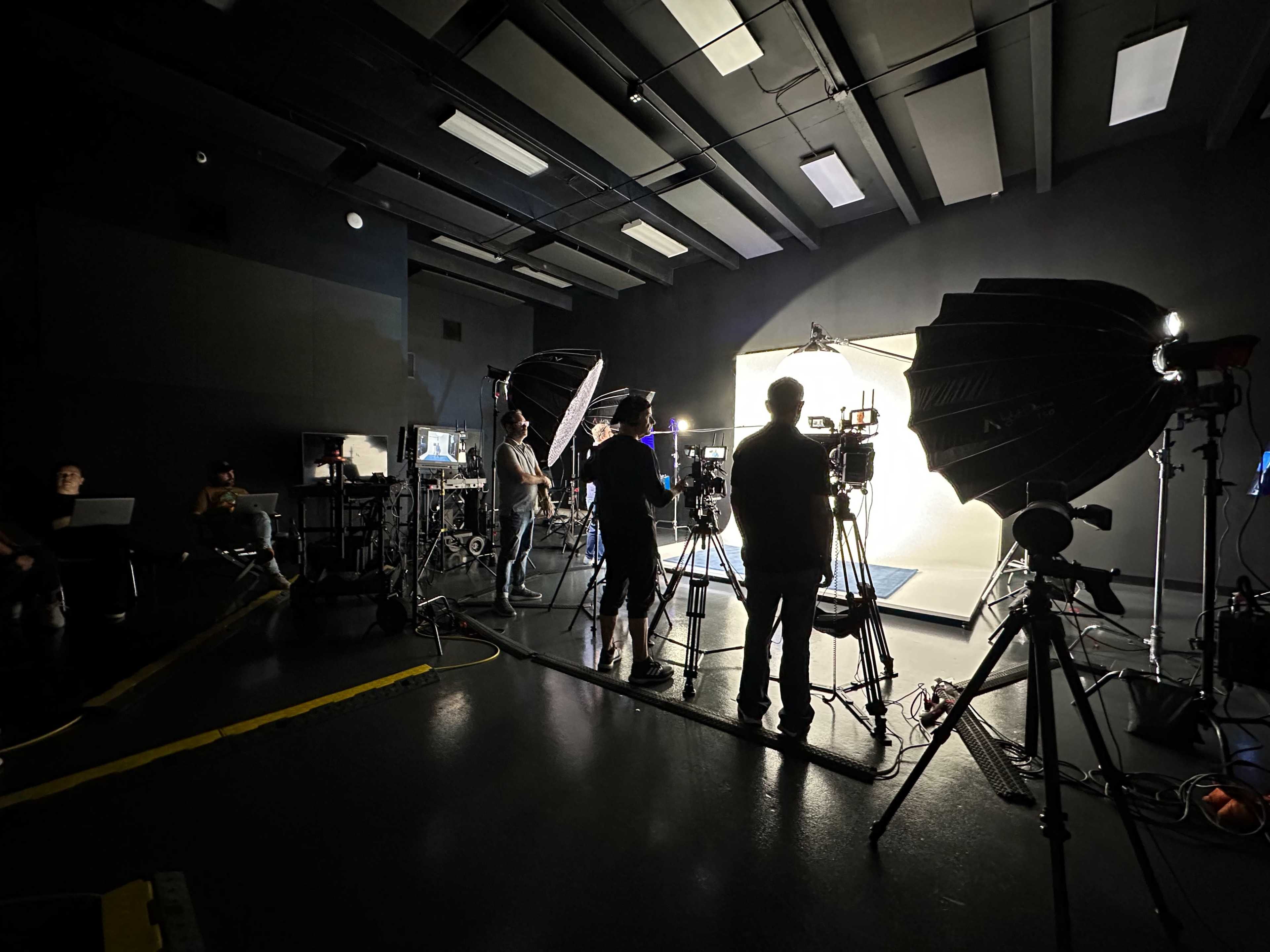 A group of people is setting up cameras and lighting equipment in a dark studio.
