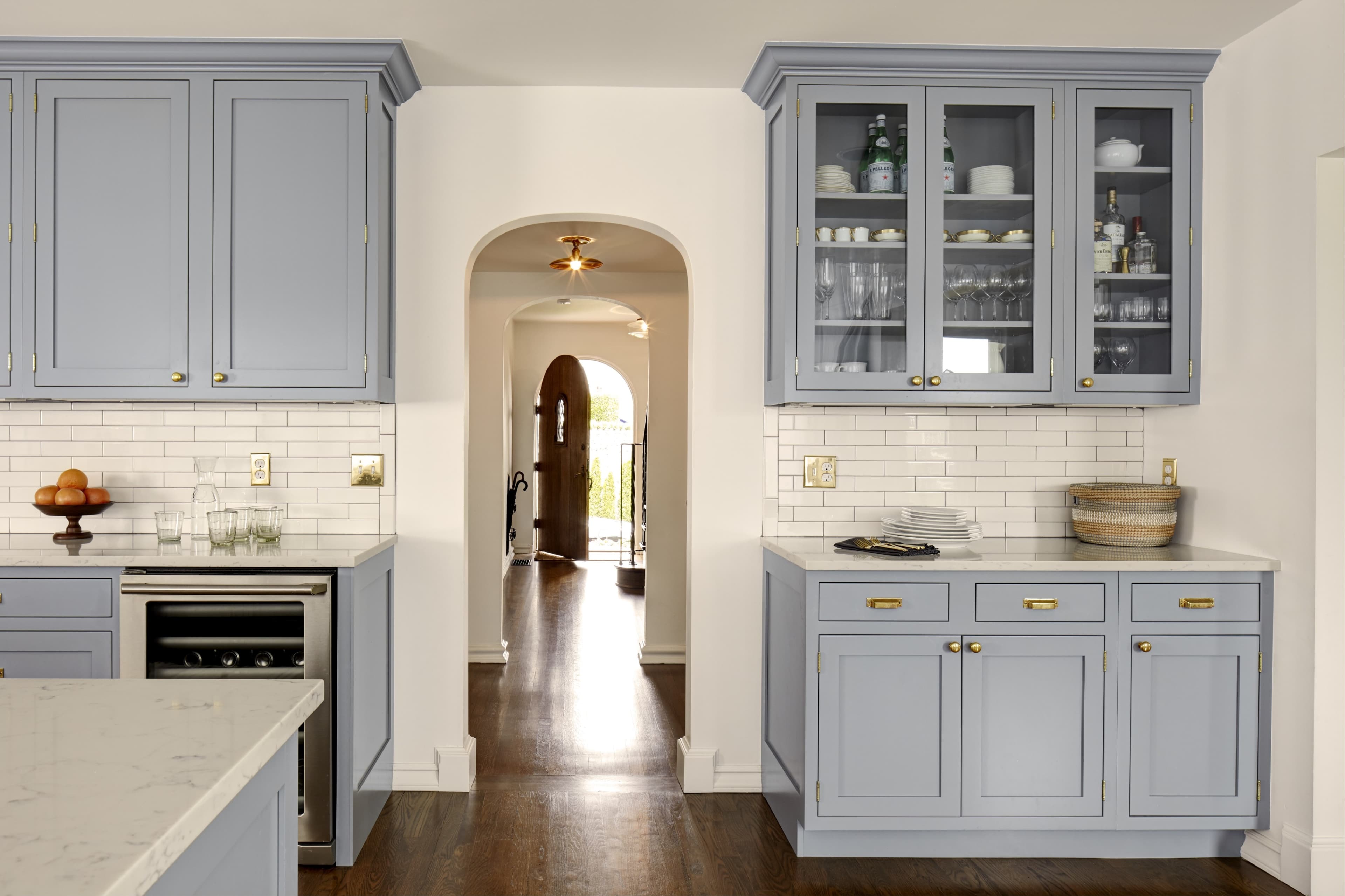 A modern kitchen featuring light blue cabinetry, white tiled backsplash, and a view of an arched entryway leading into a hallway.
