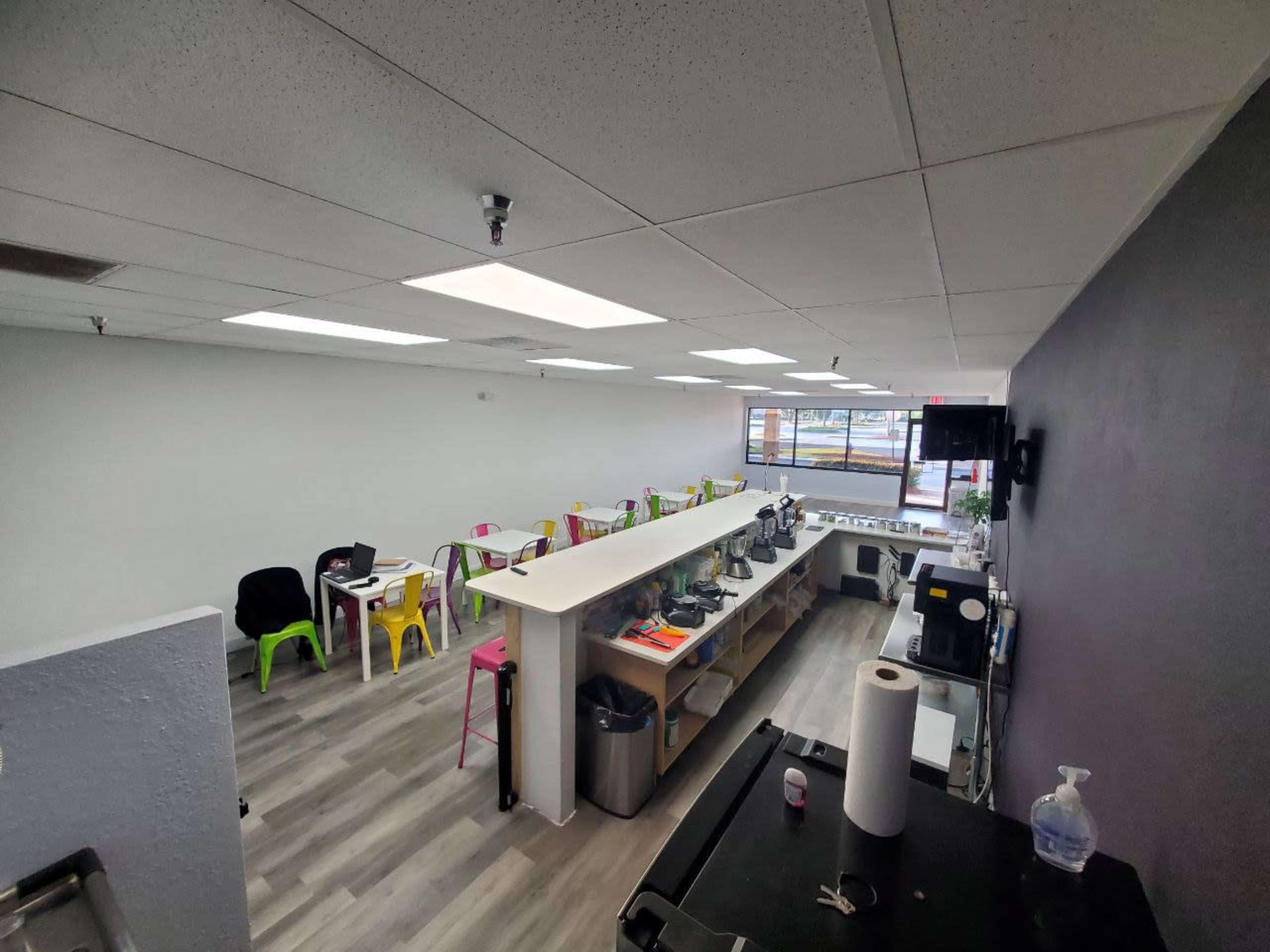 A modern, open café space with colorful chairs, a long counter, and large windows allowing natural light in.