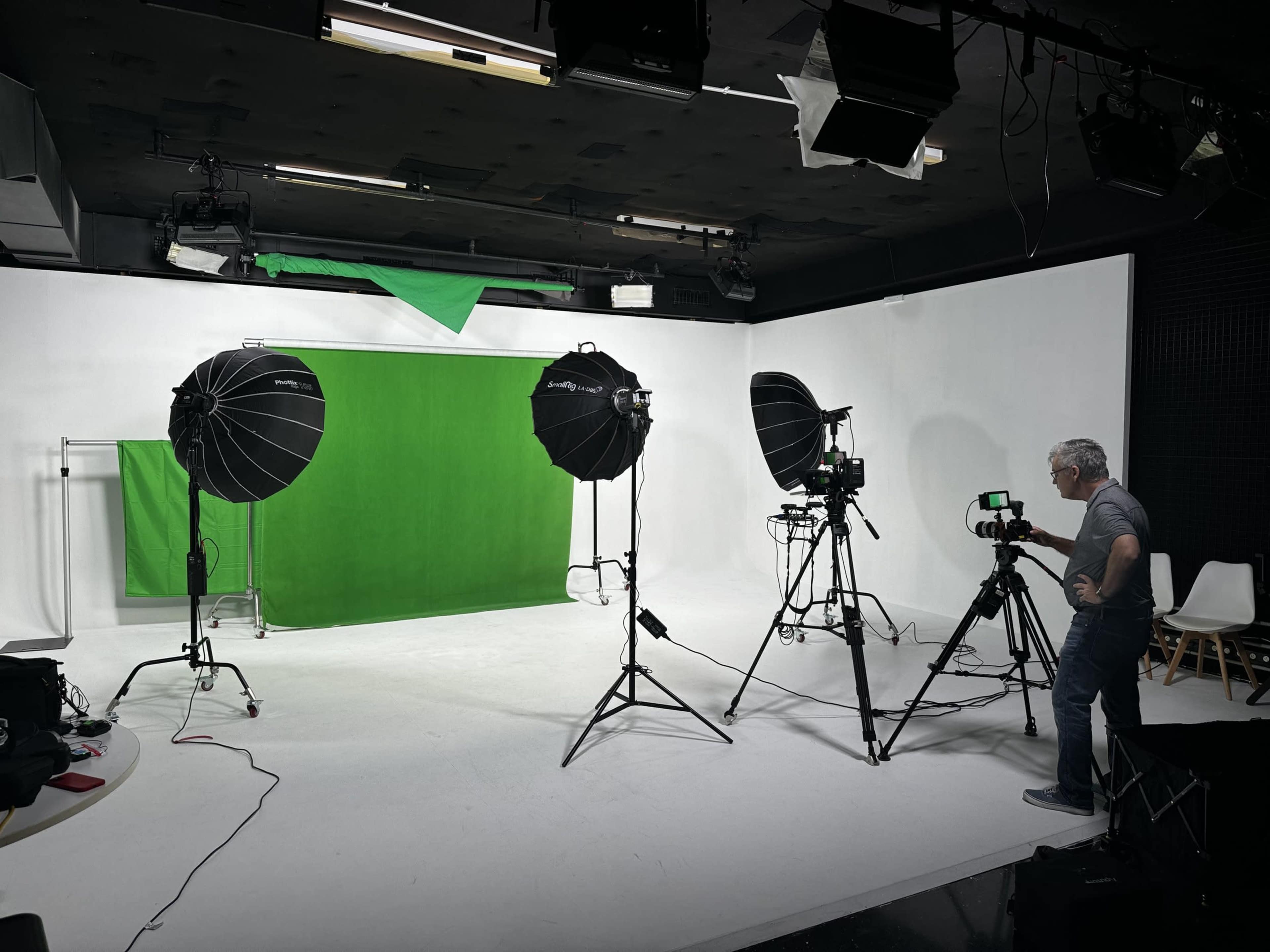 A photography studio setup features two large softbox lights and cameras positioned in front of a green backdrop.