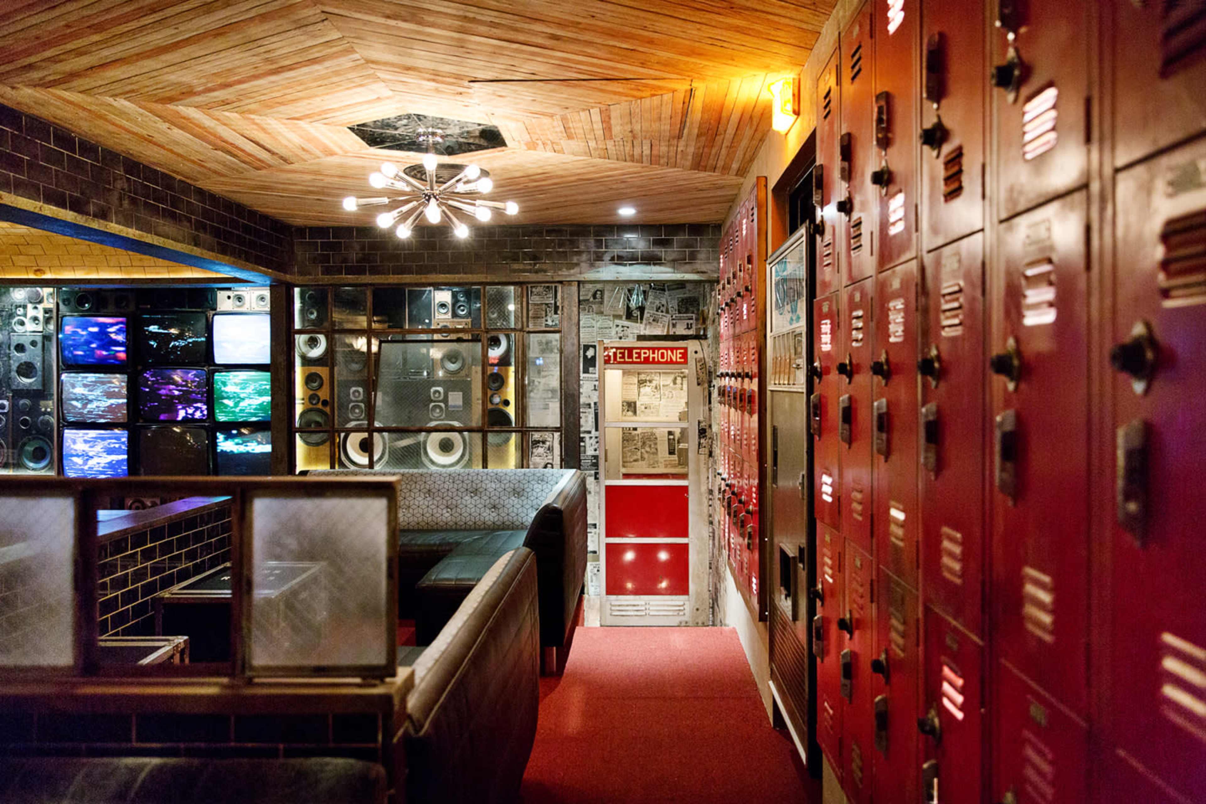 The scene features a hallway with red lockers on one side, vintage decor including wall-mounted speakers and screens, and a retro telephone booth at the end.