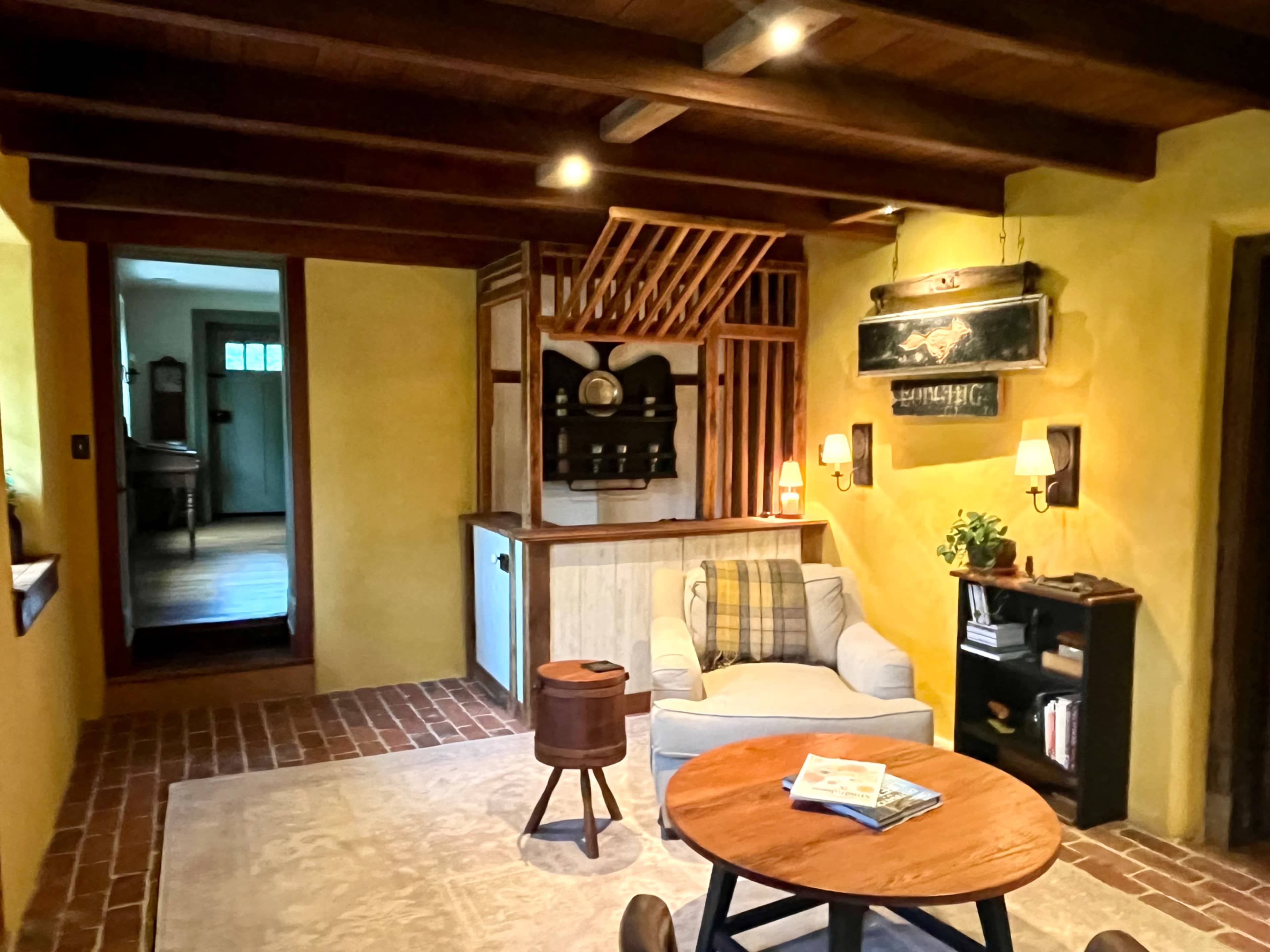The image shows a cozy living space featuring a light yellow wall, a comfortable chair, a wooden coffee table, and an open passage leading to another room.