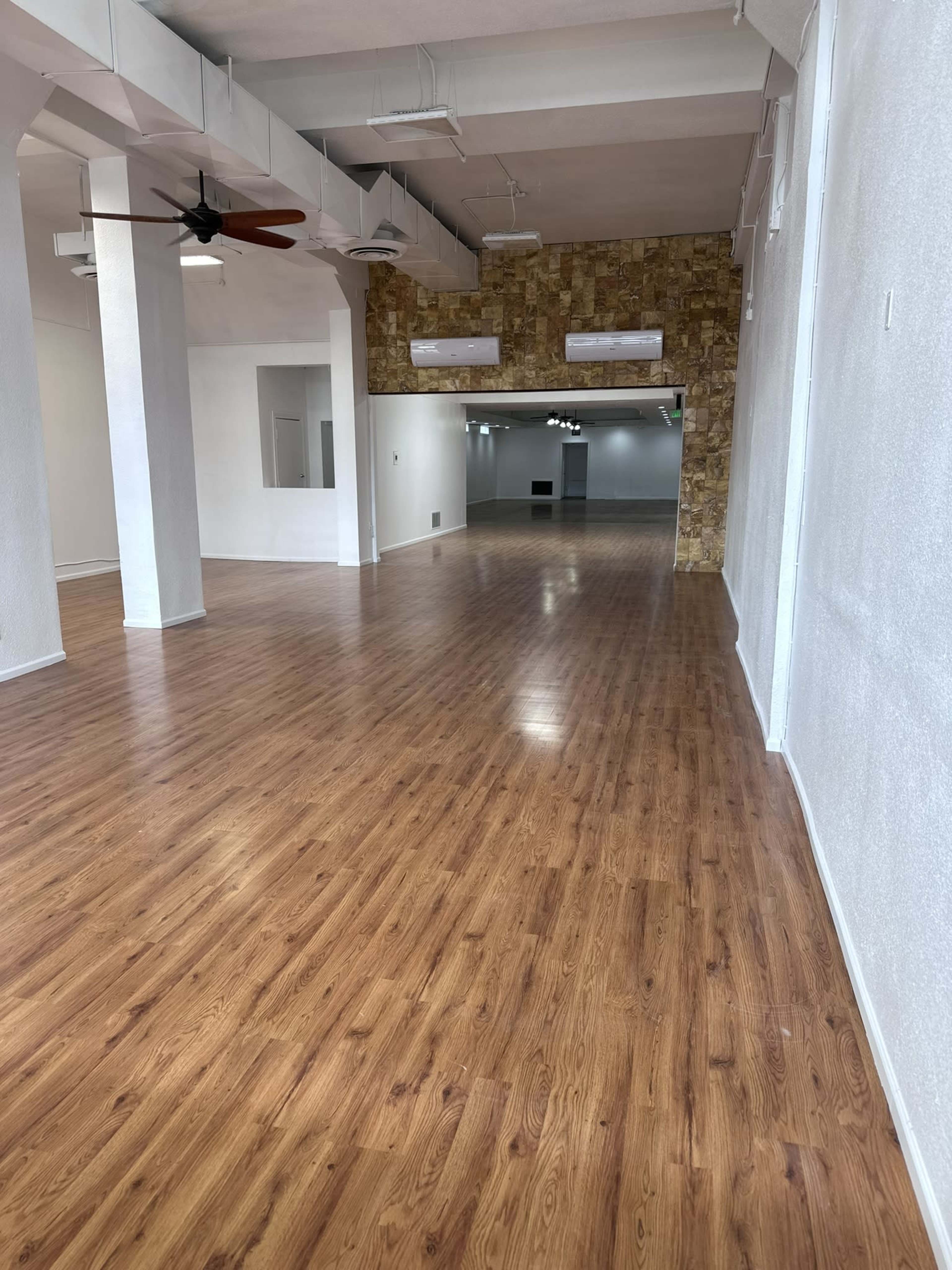 A large, empty interior space with wooden flooring and textured wall panels in the background.