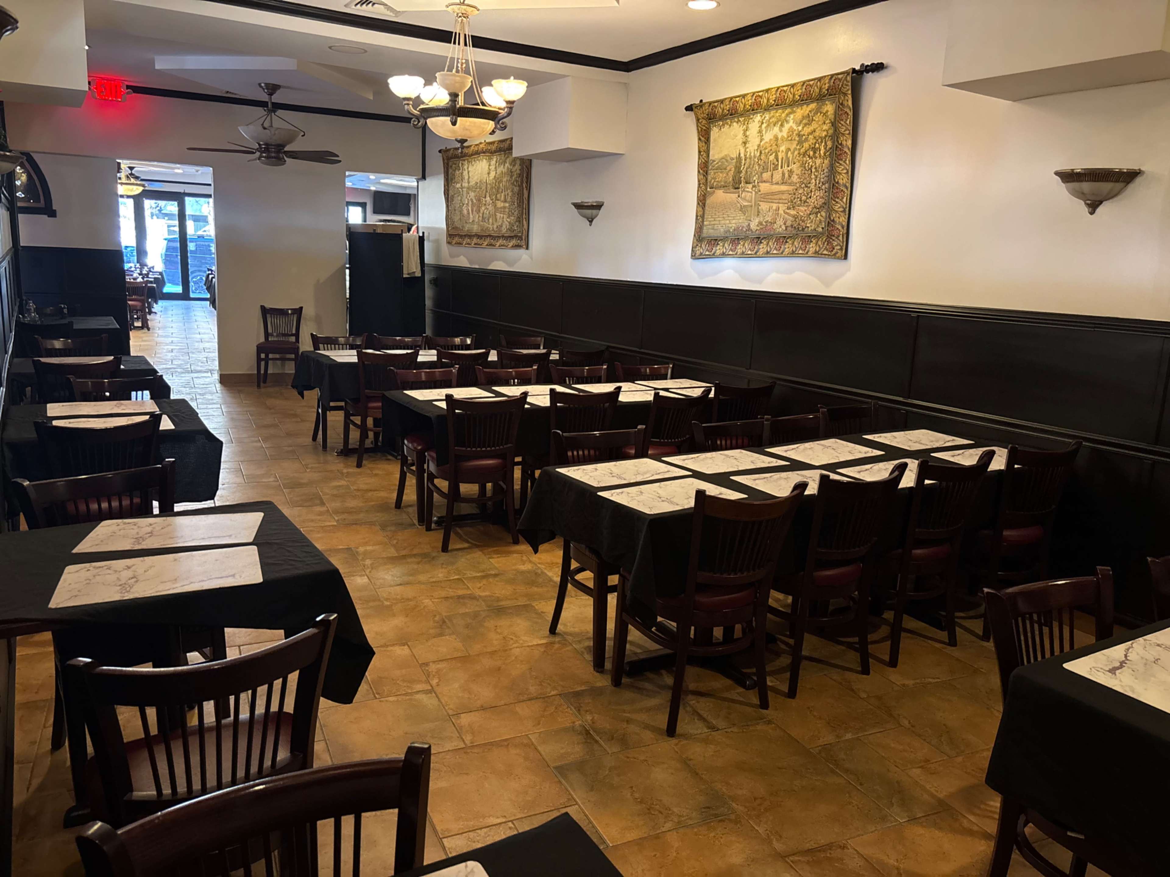 The image shows a dining area in a restaurant featuring multiple tables with black tablecloths and a tiled floor, along with wall hangings and light fixtures.