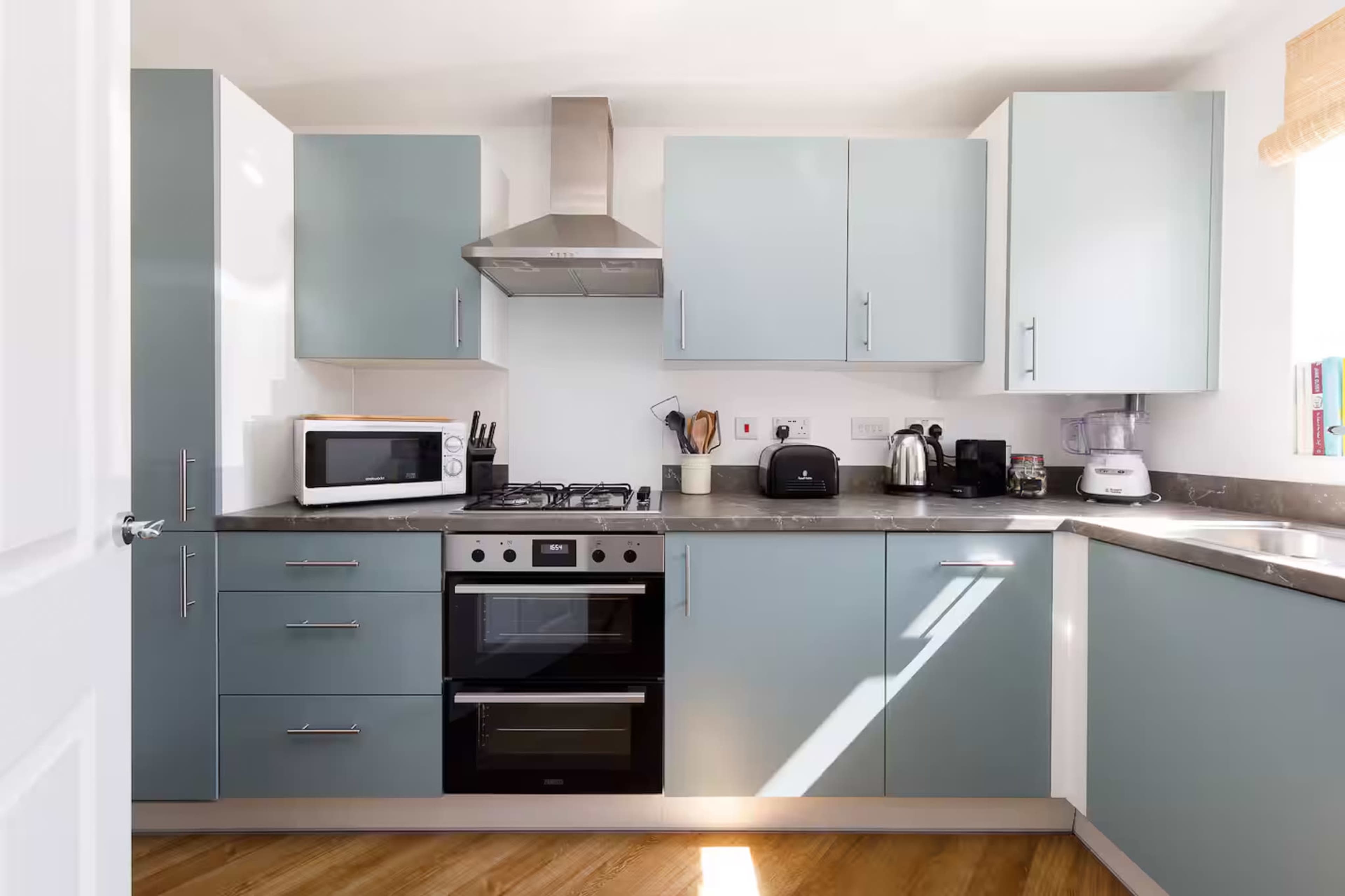 The kitchen features light blue cabinets, a stainless steel oven, and modern appliances arranged along a countertop.
