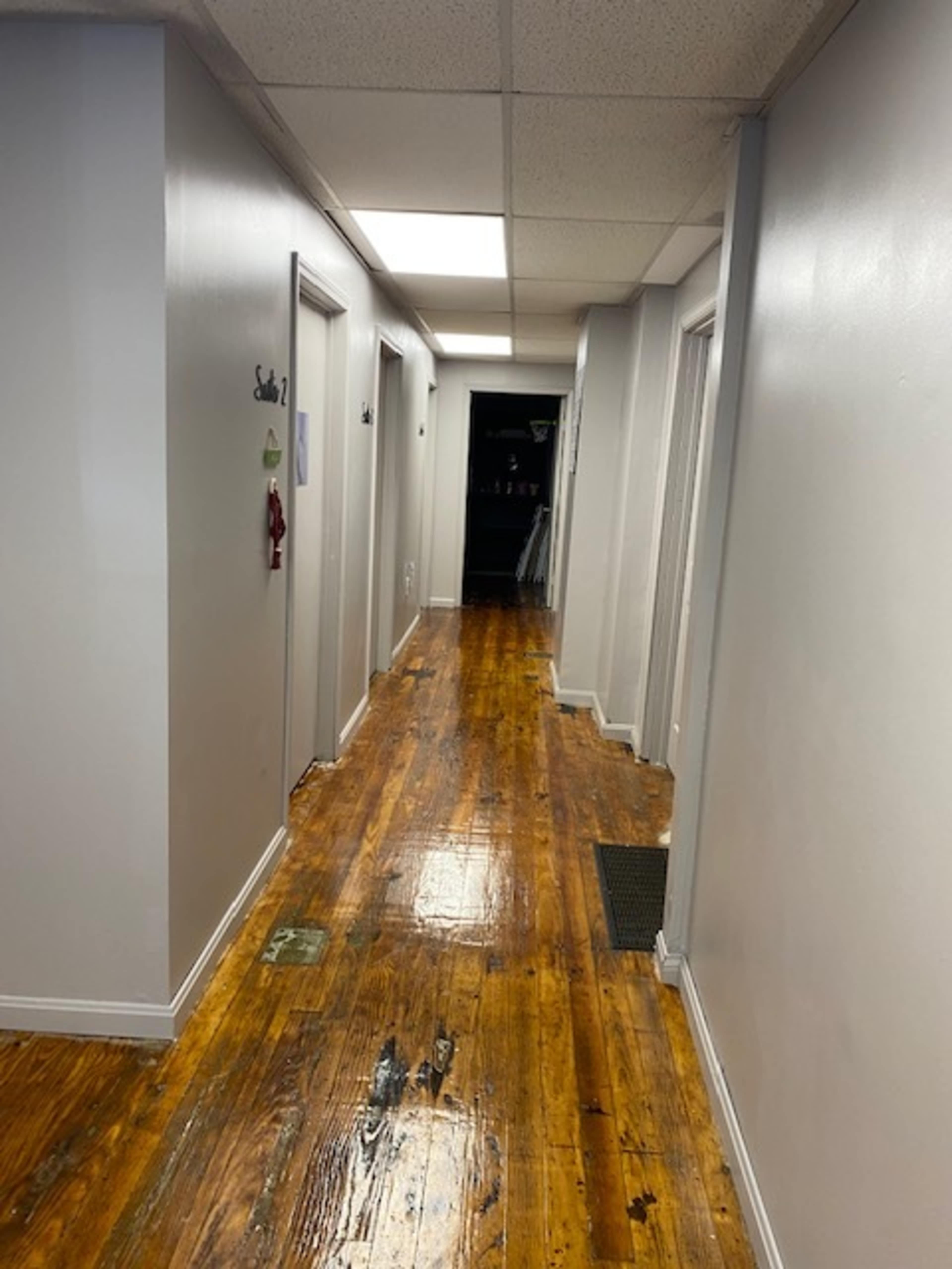 The image shows a long, narrow hallway with several closed doors on either side and a darkened area at the end.