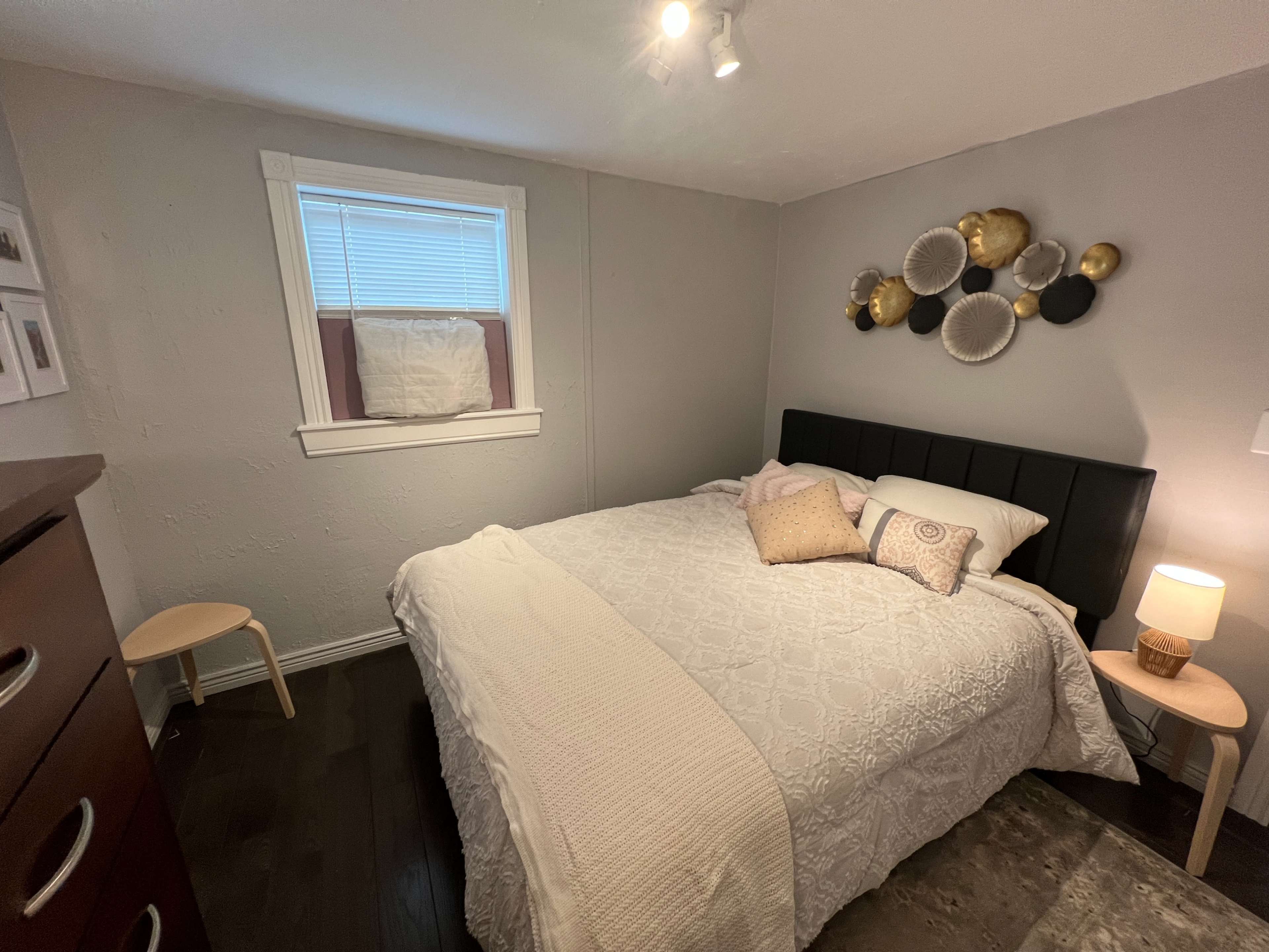 A small bedroom with a bed, a bedside lamp, a dresser, and decorative wall plates.
